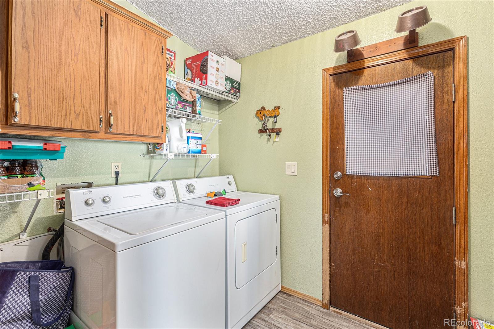 Laundry room with washer and dryer, wooden cabinets, open shelves, and a door with a checked curtain.