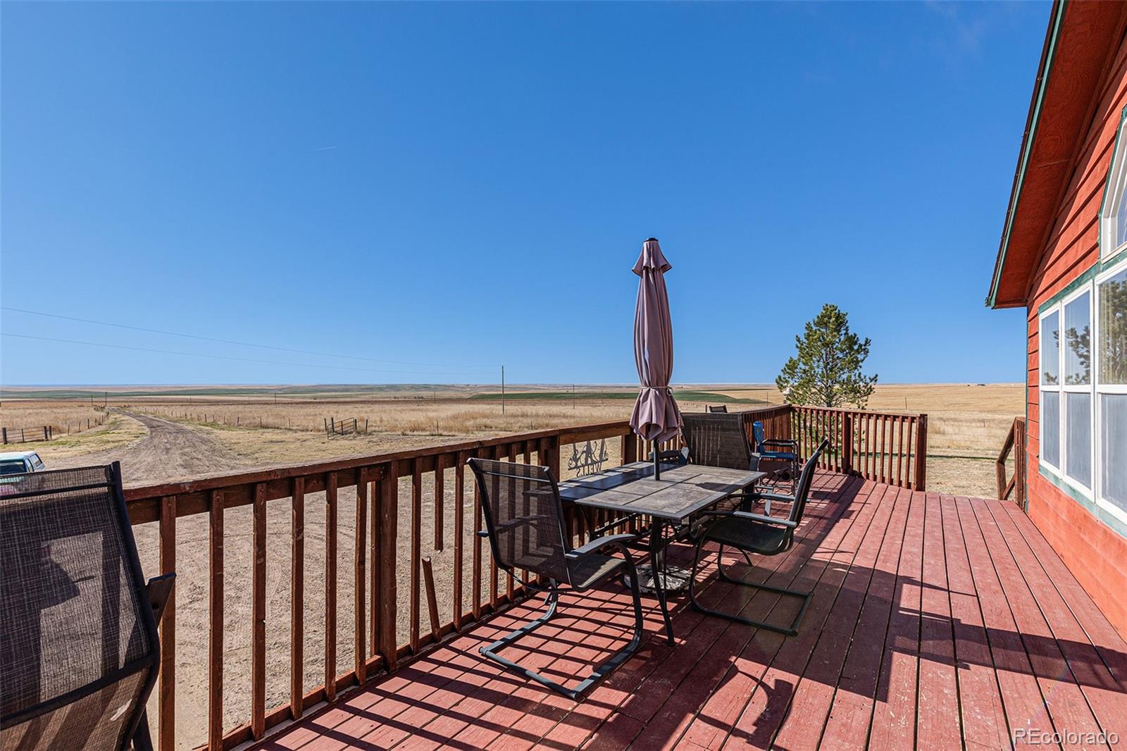 Red wooden deck with outdoor dining furniture overlooking open grassland.