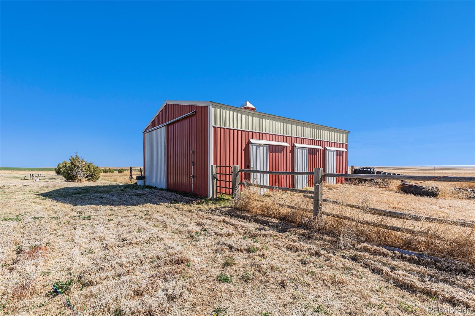 Red and cream metal barn with three side doors in an open rural field.