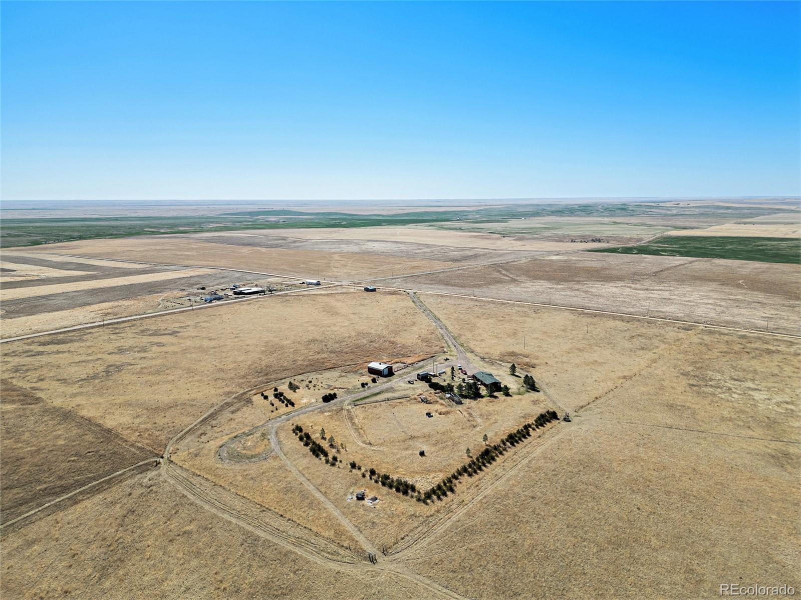 Aerial view of a rural property with scattered buildings, a tree-lined yard, and open fields.