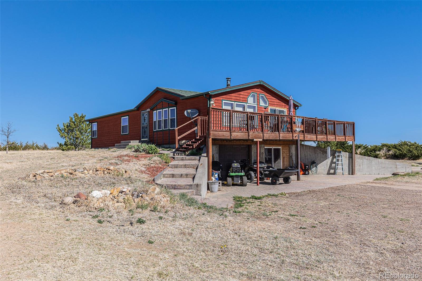 Red-sided home with a raised deck and open garage on a dry, sloping lot.