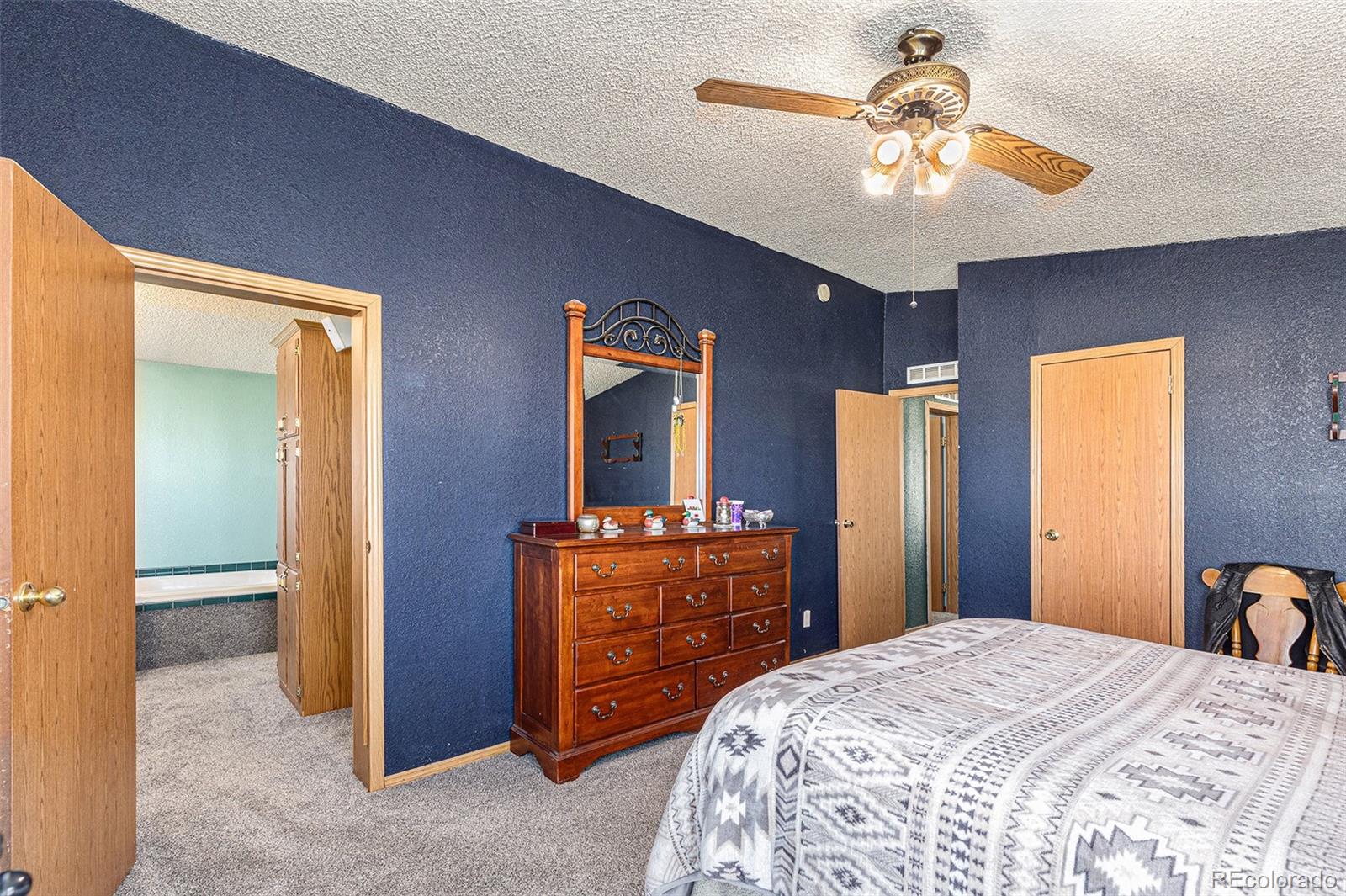 Bedroom with dark blue walls, wooden dresser and mirror, and an open doorway to a bathroom.