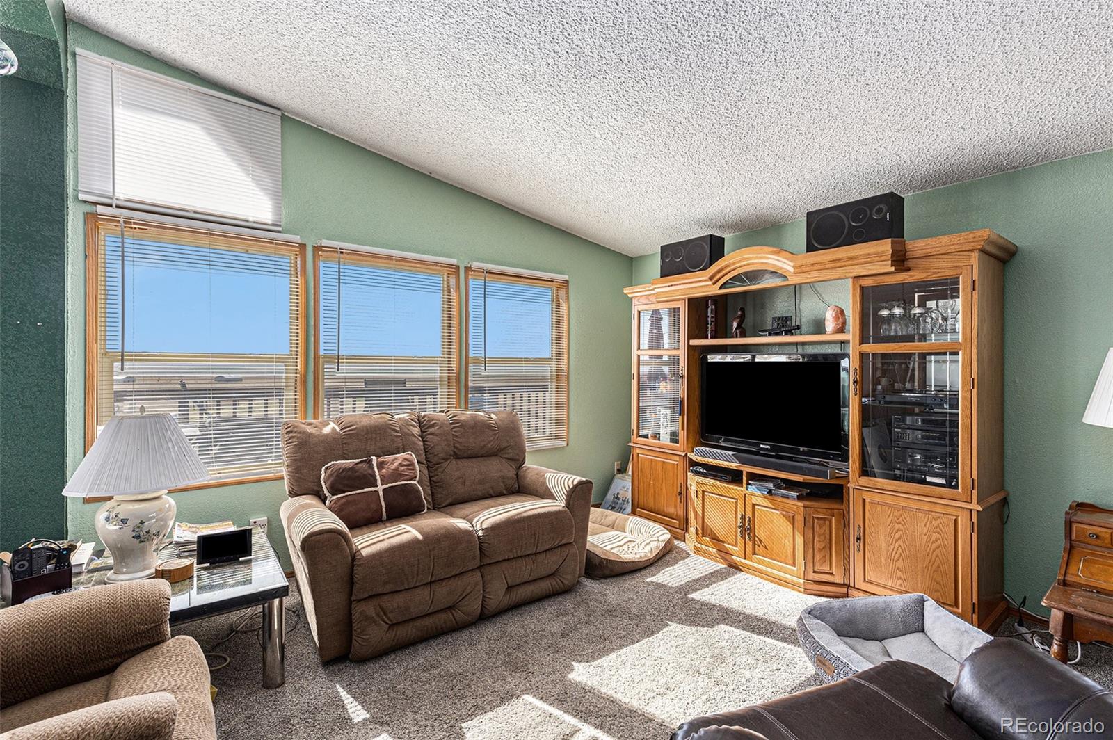 Living room with green walls, sunlit windows, a brown reclining sofa, and a large wooden entertainment center.