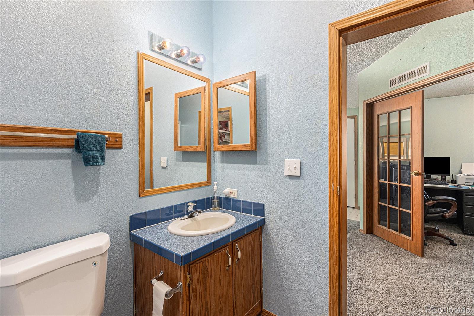 Bathroom vanity with blue tile and wood cabinetry beside an open doorway to an office.