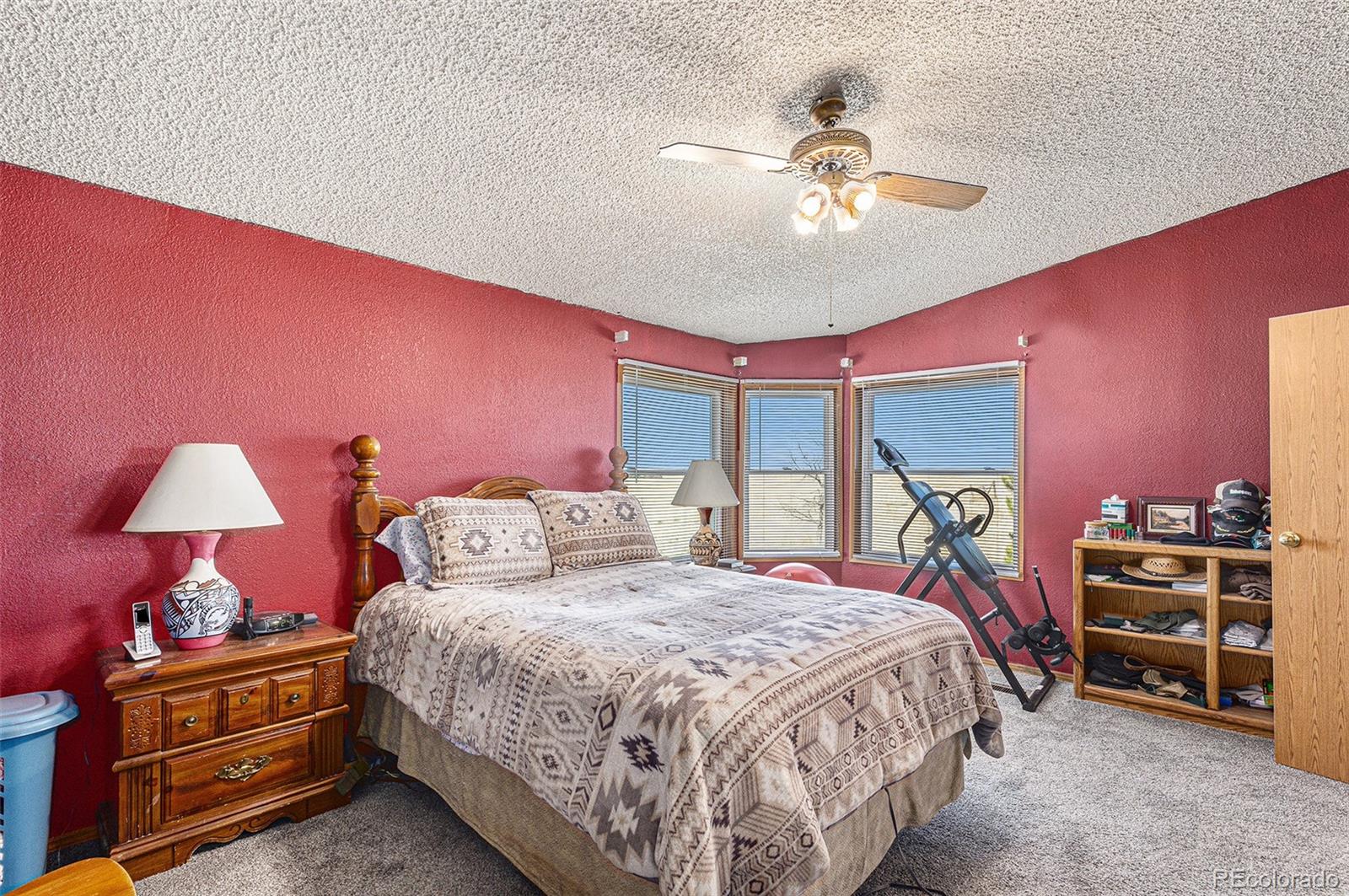 Bedroom with red walls, a patterned bed, bay windows, and an exercise machine.
