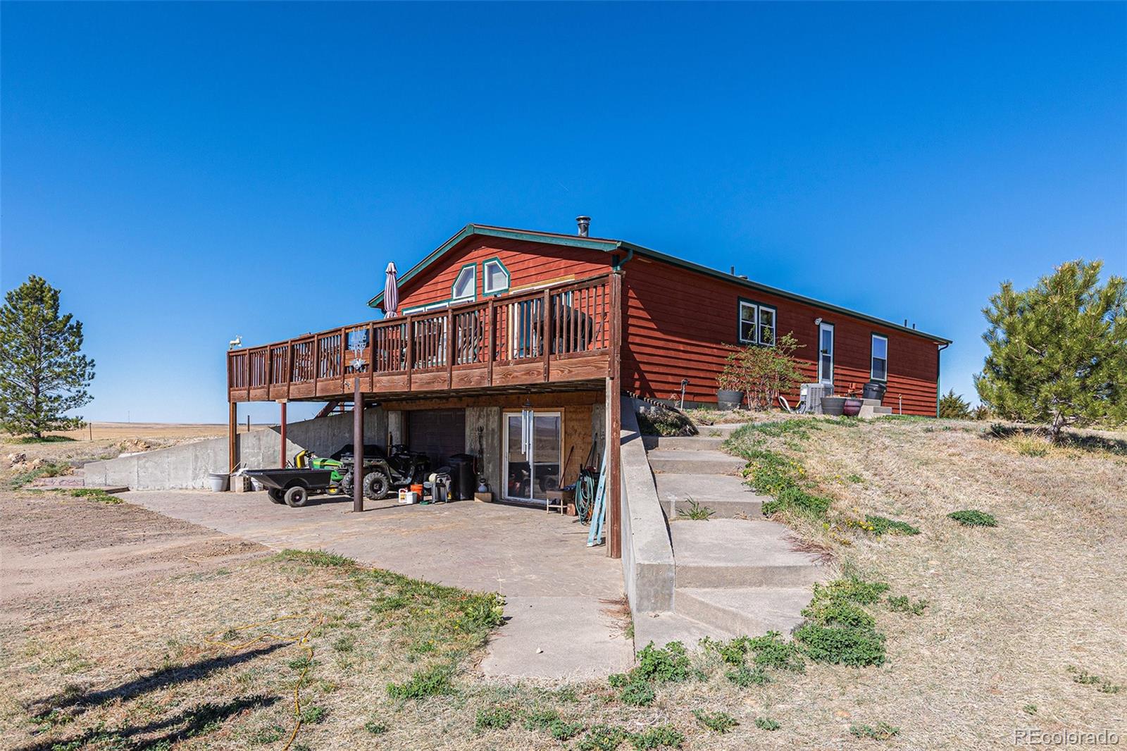 Red-sided raised home with a broad wooden deck and exposed lower-level patio area.