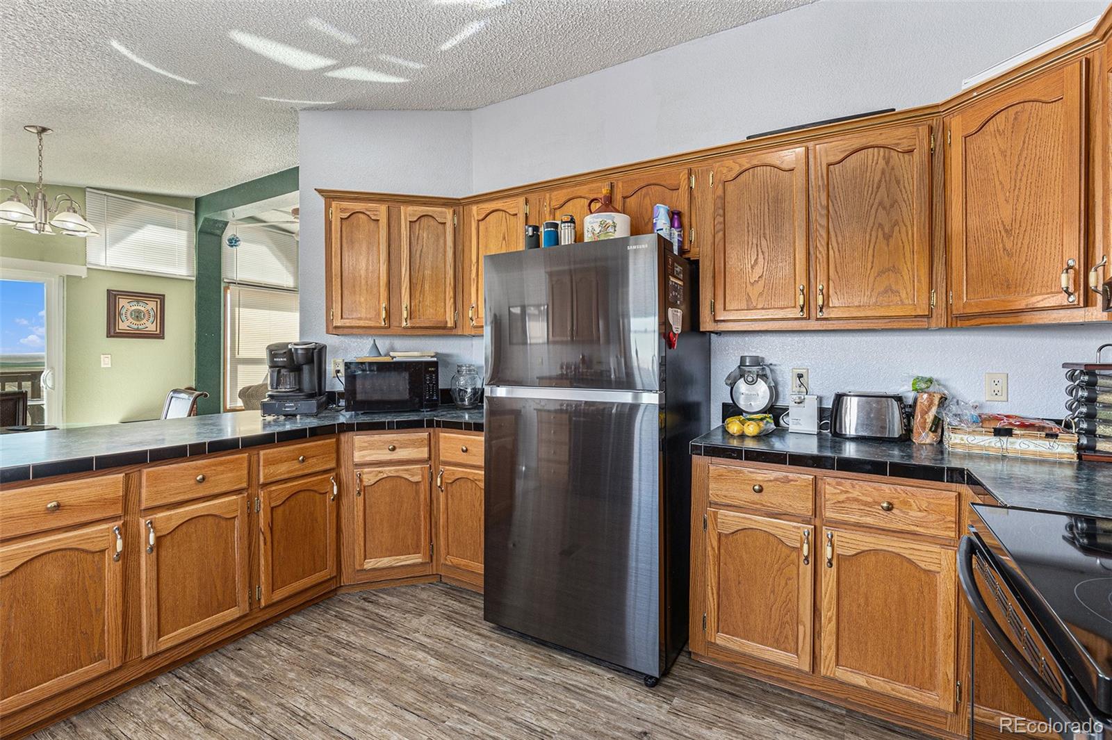 Kitchen with honey-toned wood cabinets, dark countertops, and a stainless steel refrigerator.