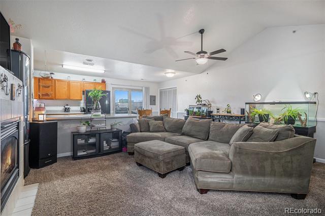 Living room with a gray sectional and ottoman beside an open kitchen with orange cabinets.