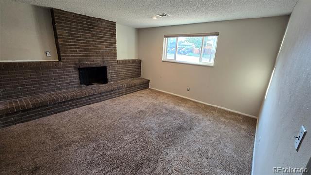 Vacant living room with a brick fireplace, raised hearth, brown carpet, and a window.