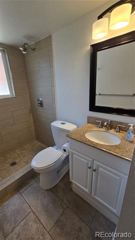 Bathroom with a tiled shower, small window, white vanity, and dark-framed mirror.