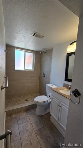 Bathroom with a tiled walk-in shower, frosted window, toilet, and white vanity.