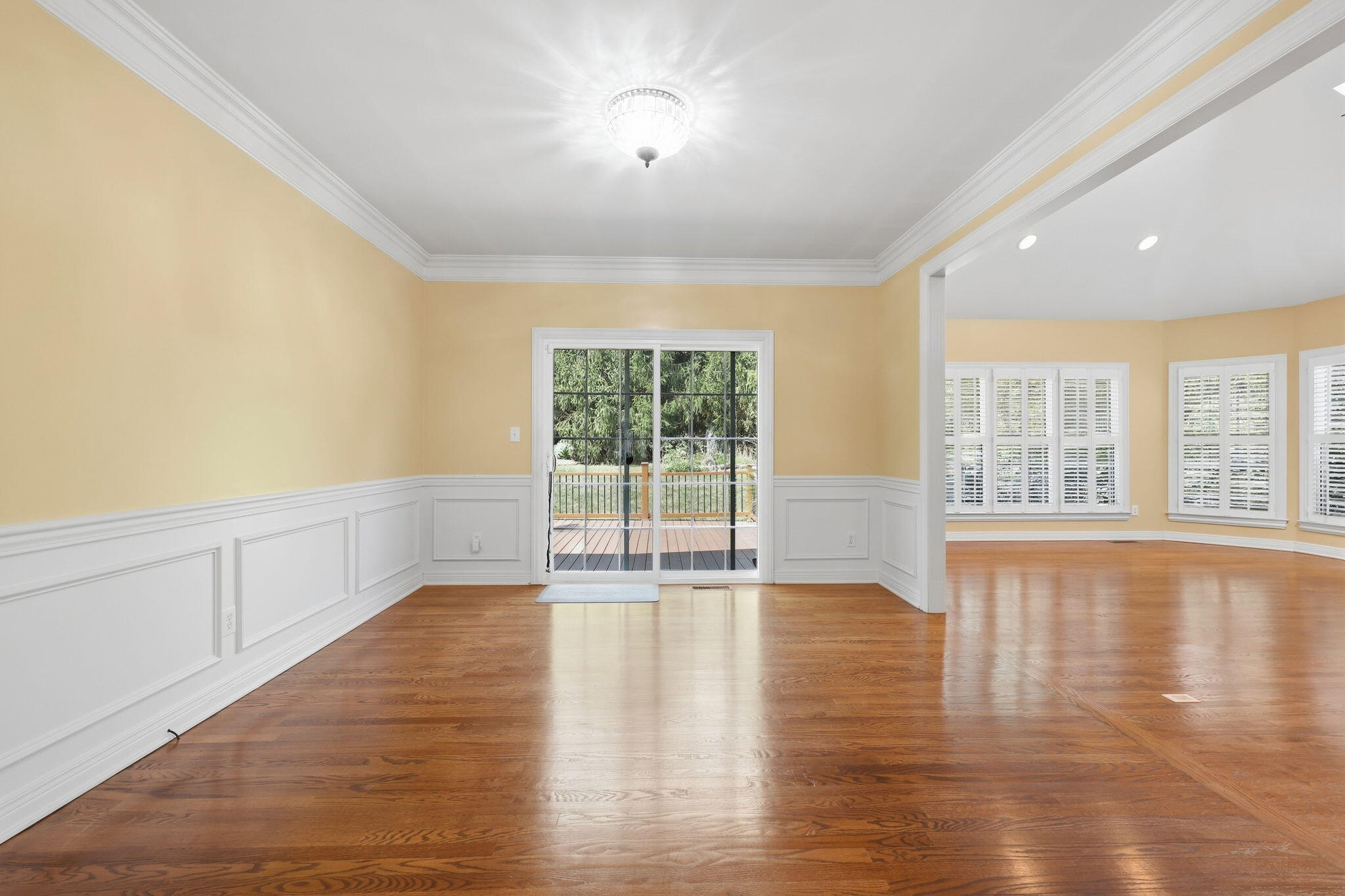 Empty room with hardwood floors, paneled wainscoting, and a sliding glass door to the deck.
