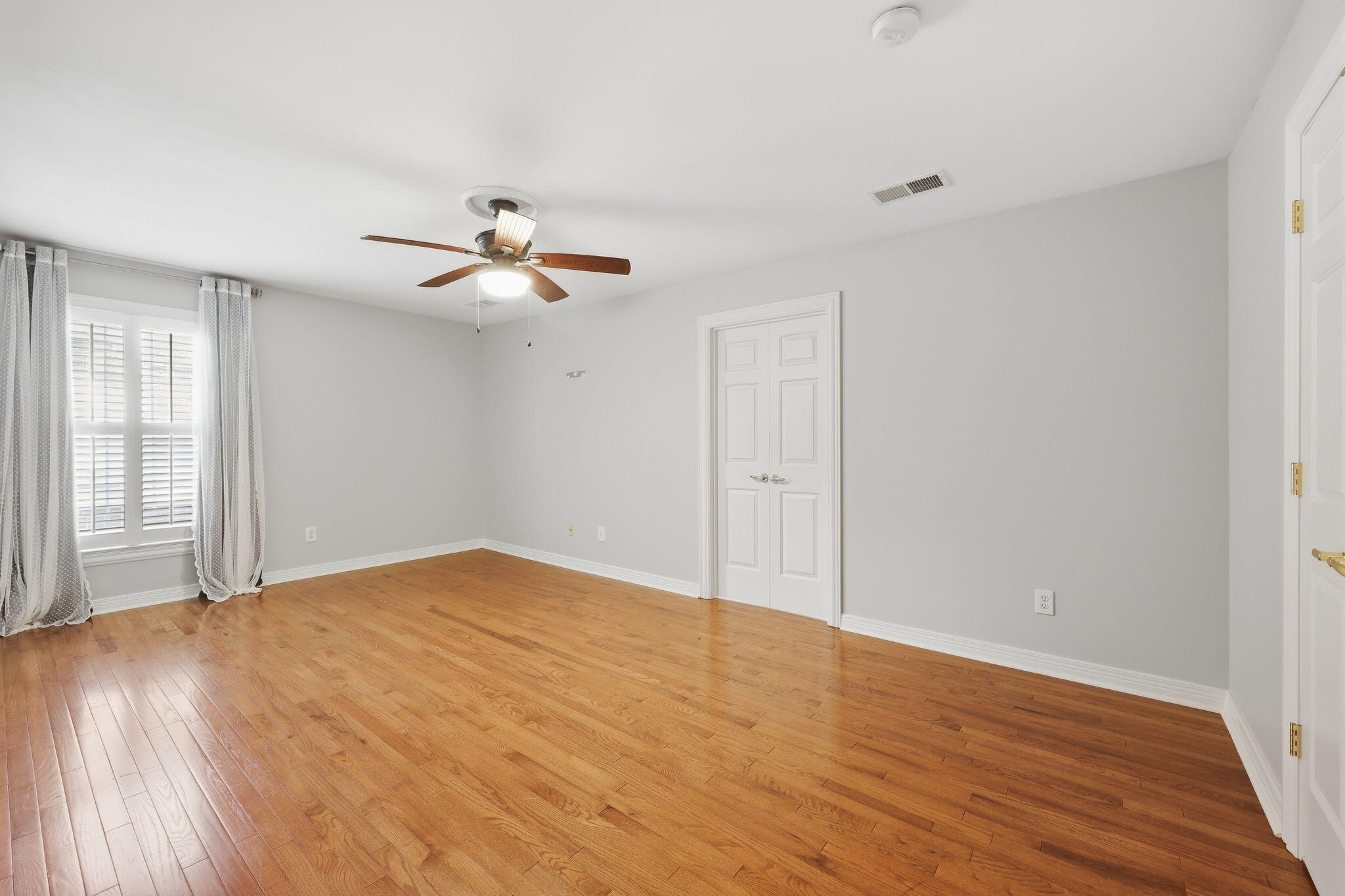 Empty bedroom with hardwood floors, a ceiling fan, and a shuttered window.
