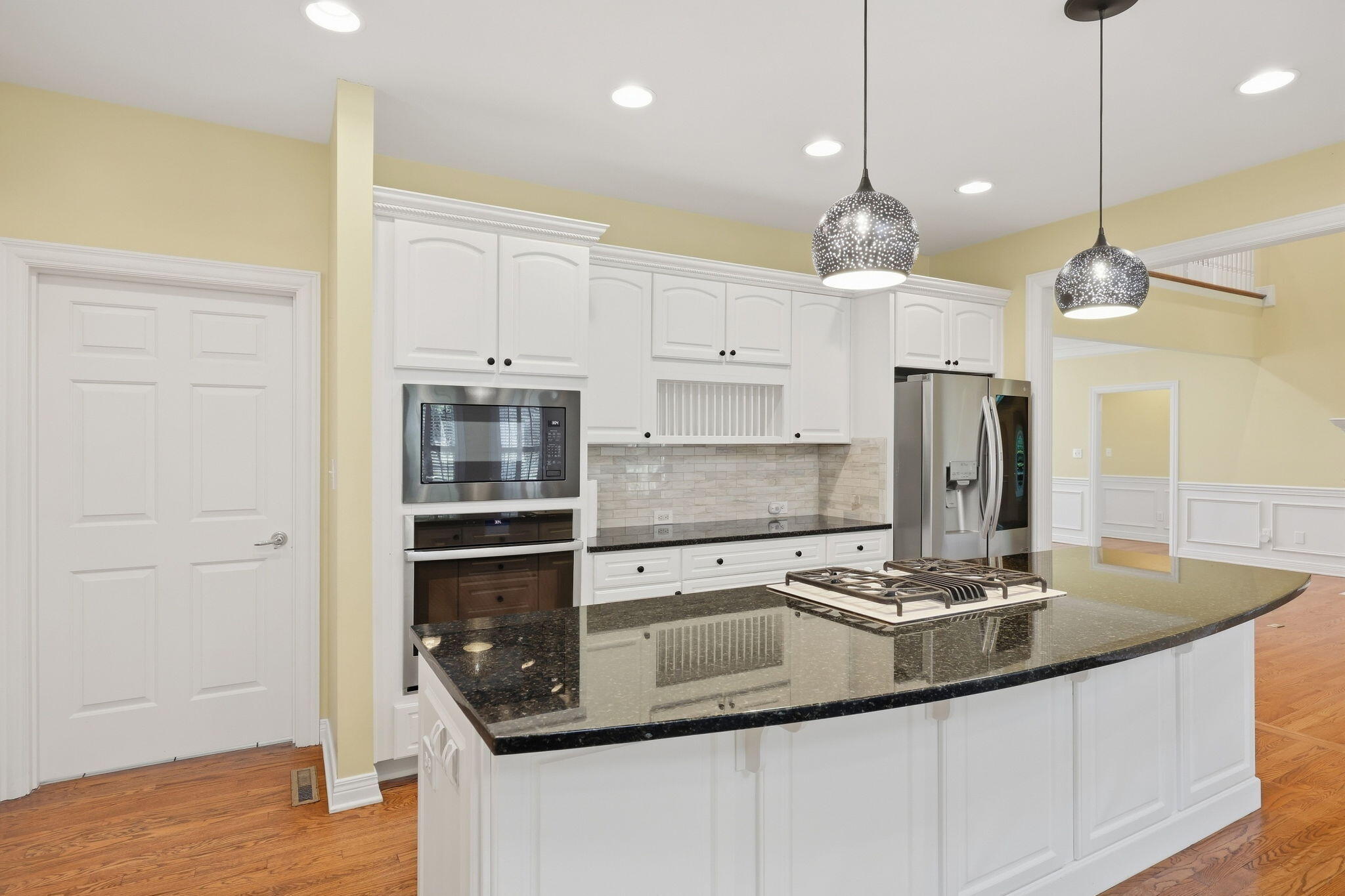 Kitchen with a black granite island and gas cooktop, white cabinetry, and stainless steel appliances.
