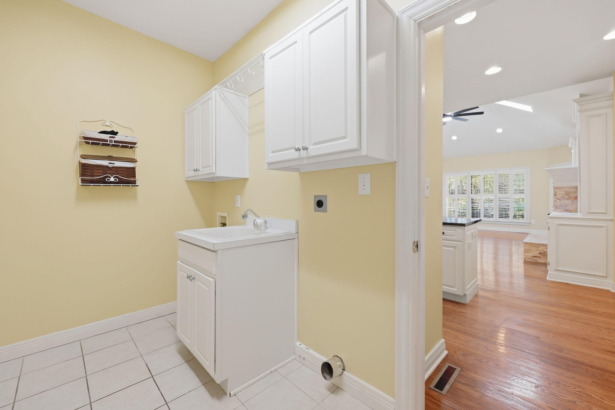 Laundry room with white utility sink and cabinets, opening onto a hardwood-floored living area.