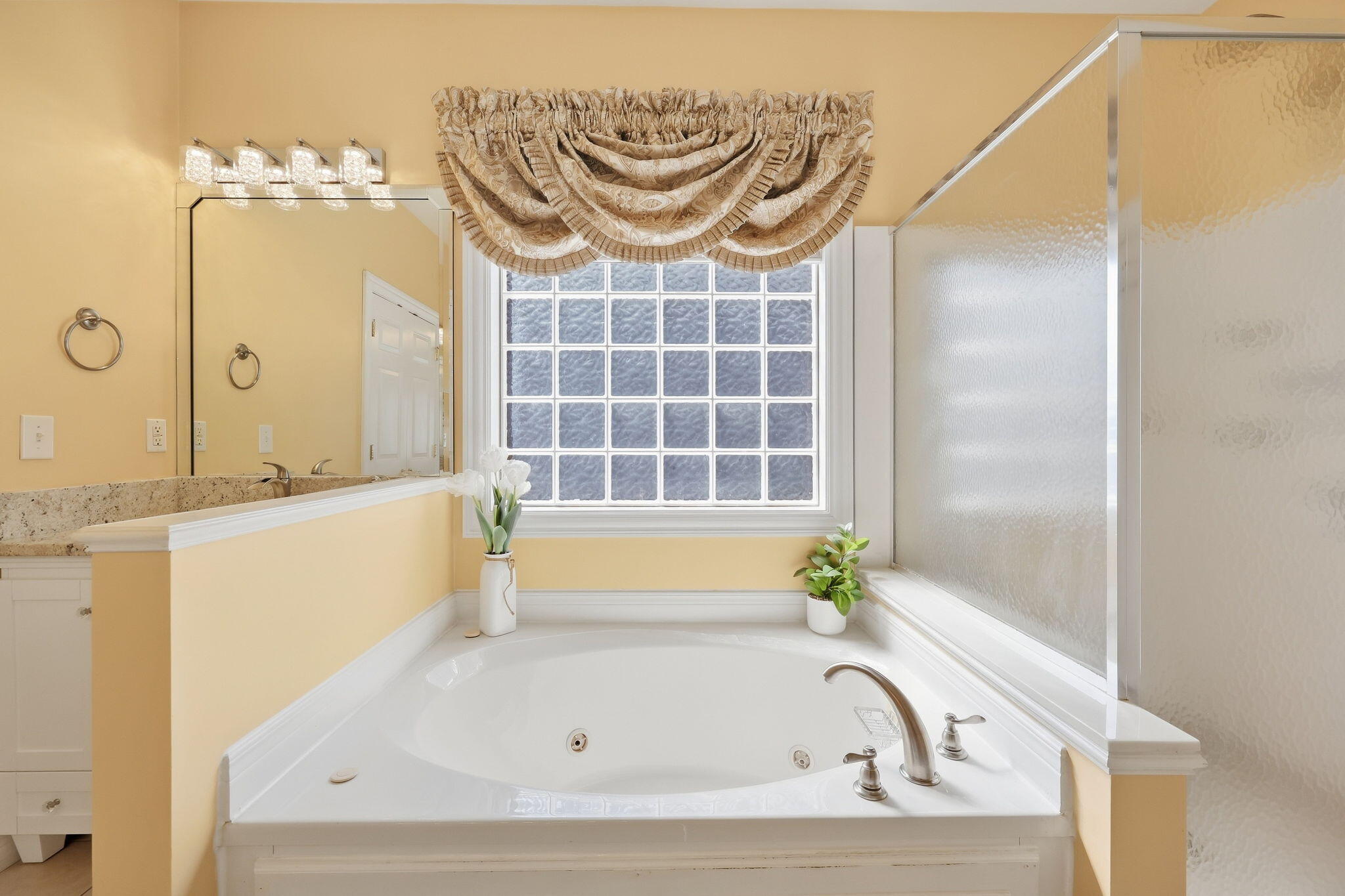 Bathroom with a jetted soaking tub beneath a glass-block window and an adjacent glass shower.