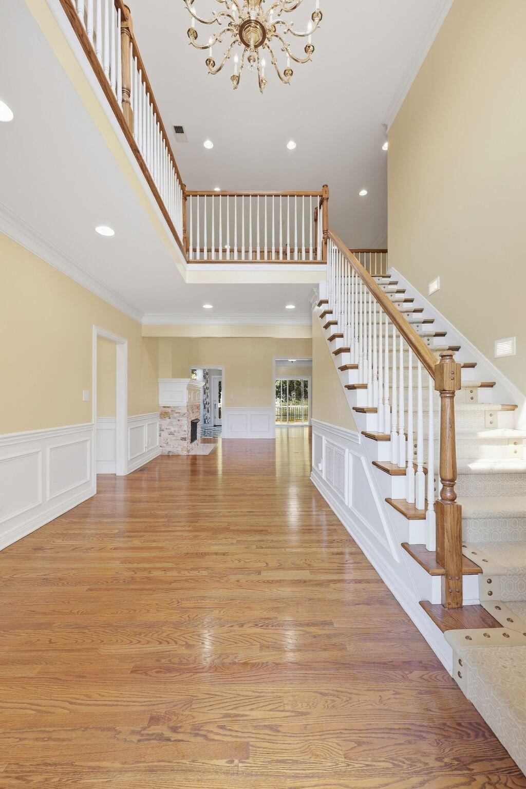 Two-story foyer with a carpeted staircase, wood handrails, polished hardwood floors, and a chandelier.