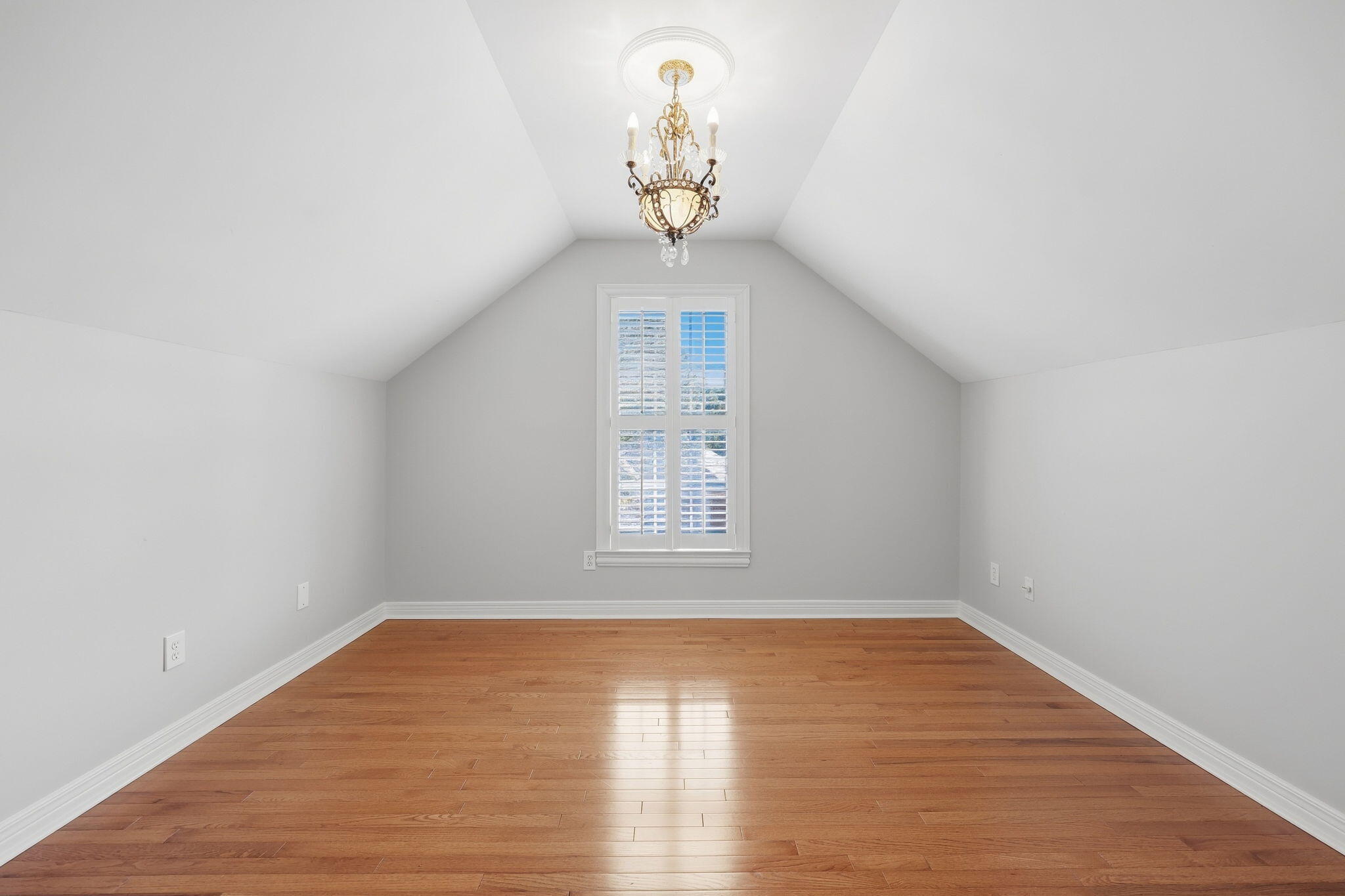 Empty vaulted room with hardwood floors, a chandelier, and a shuttered window.
