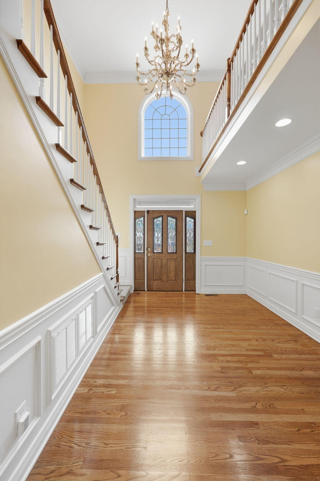 Two-story entry foyer with a chandelier, sweeping staircase, arched window, and hardwood floors.
