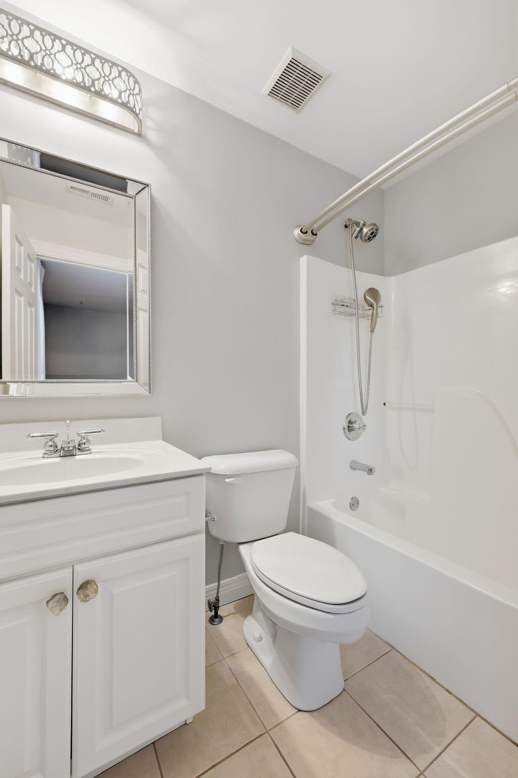 Bathroom with a white tub and shower, toilet, vanity, and large framed mirror.