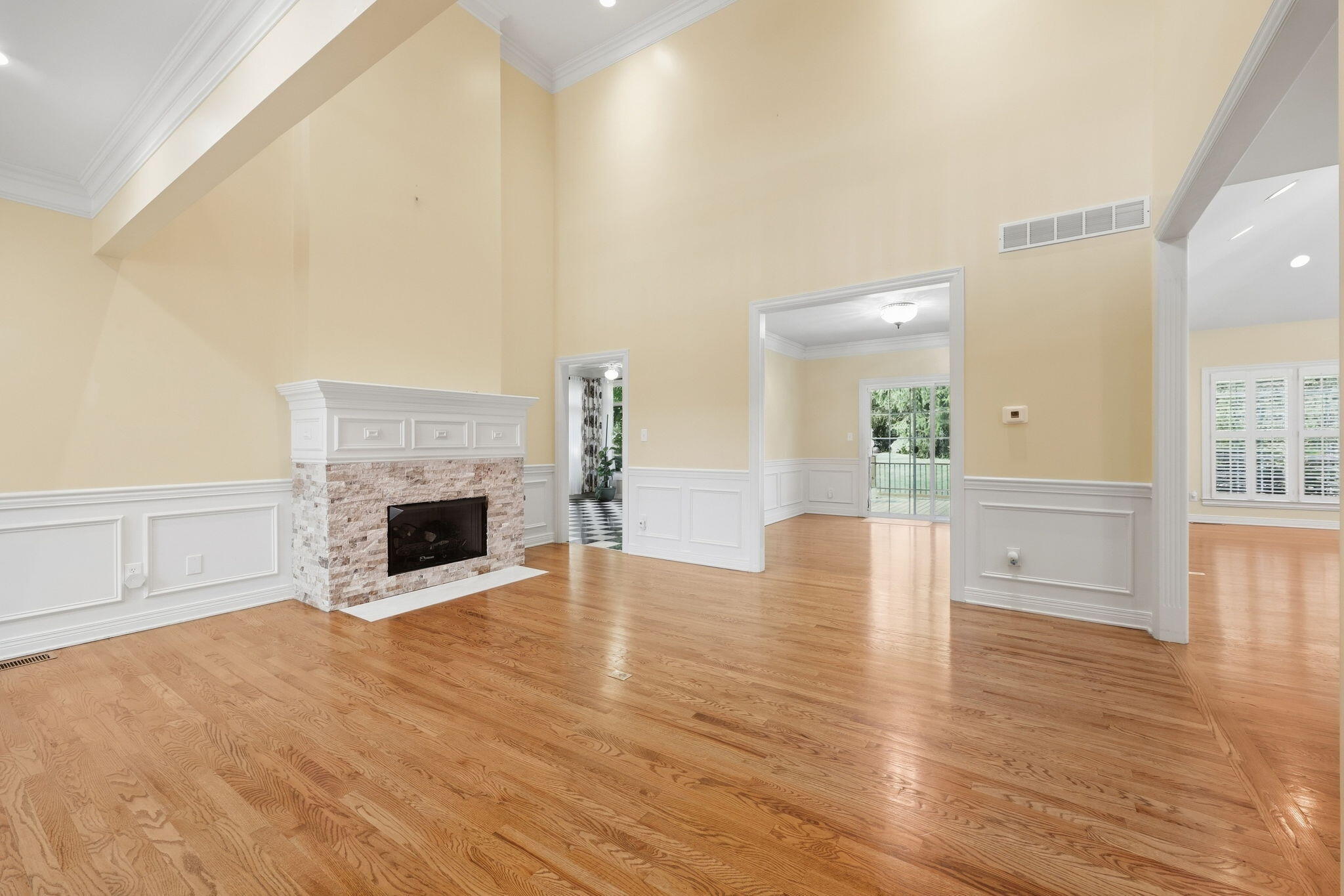 Unfurnished living room with hardwood floors, white wainscoting, and a stone fireplace.