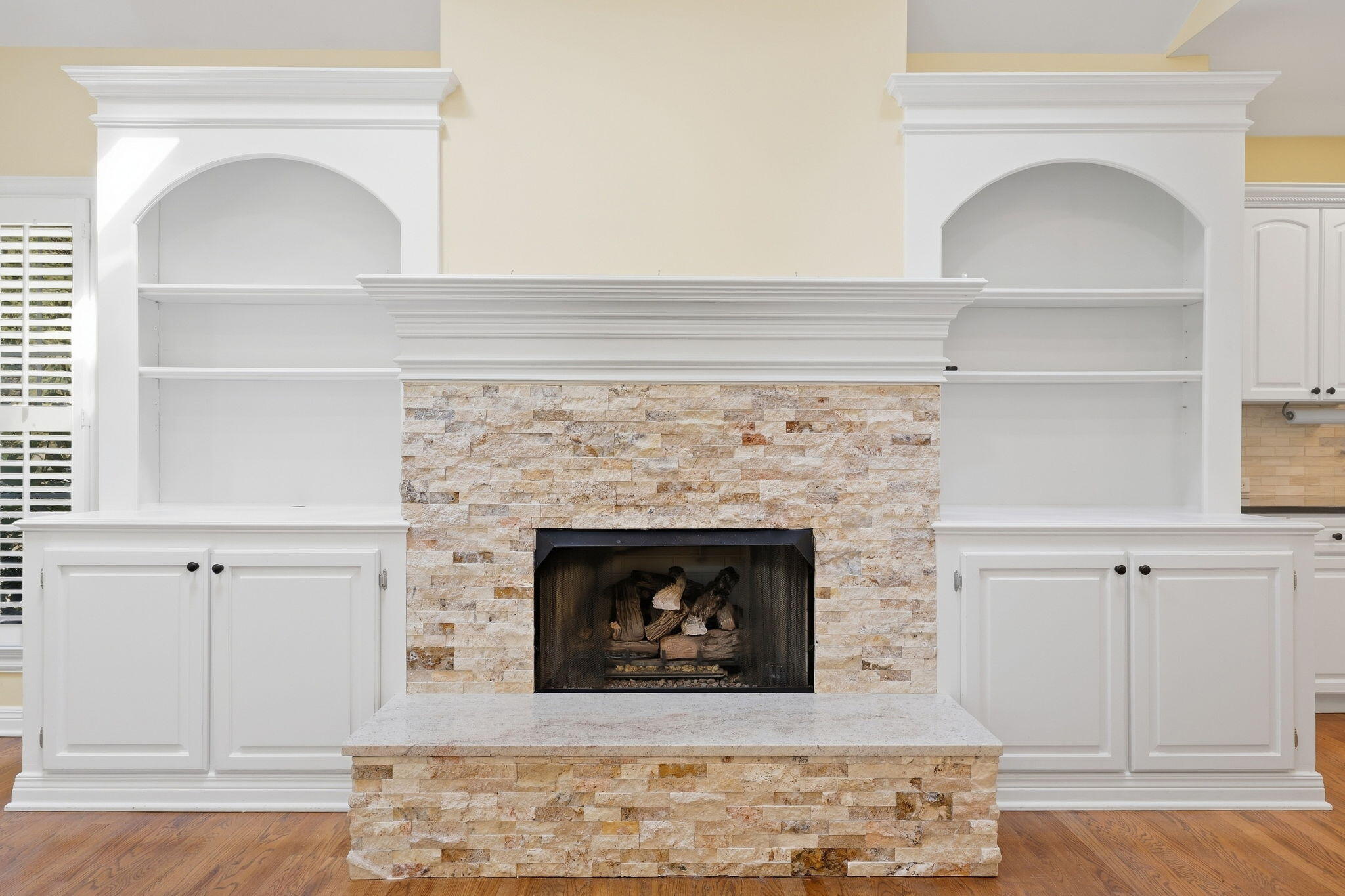 Living room fireplace with a stone surround, white built-ins, and hardwood floors.
