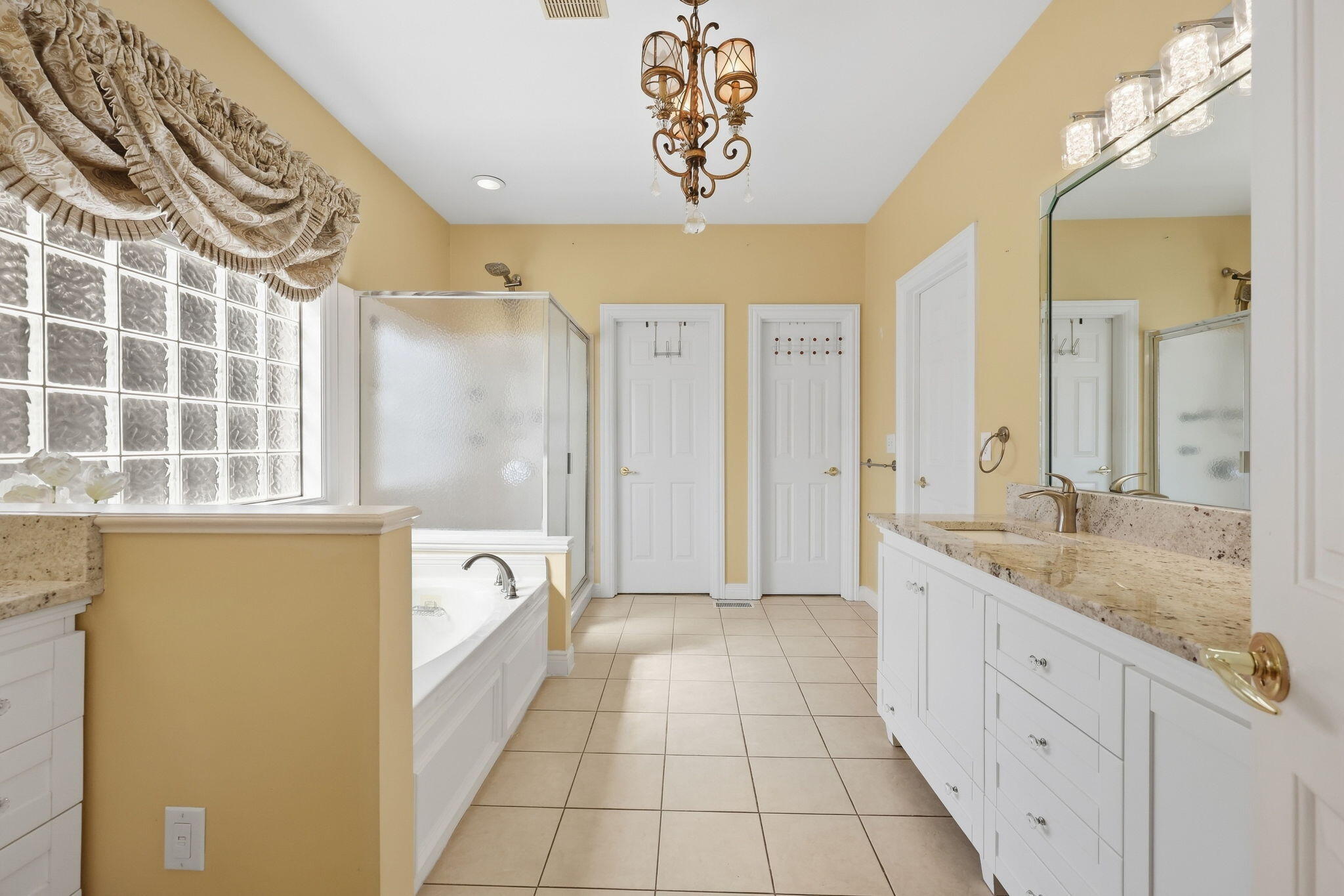 Bathroom with a granite double vanity, glass-block window, tiled shower, and corner bathtub.