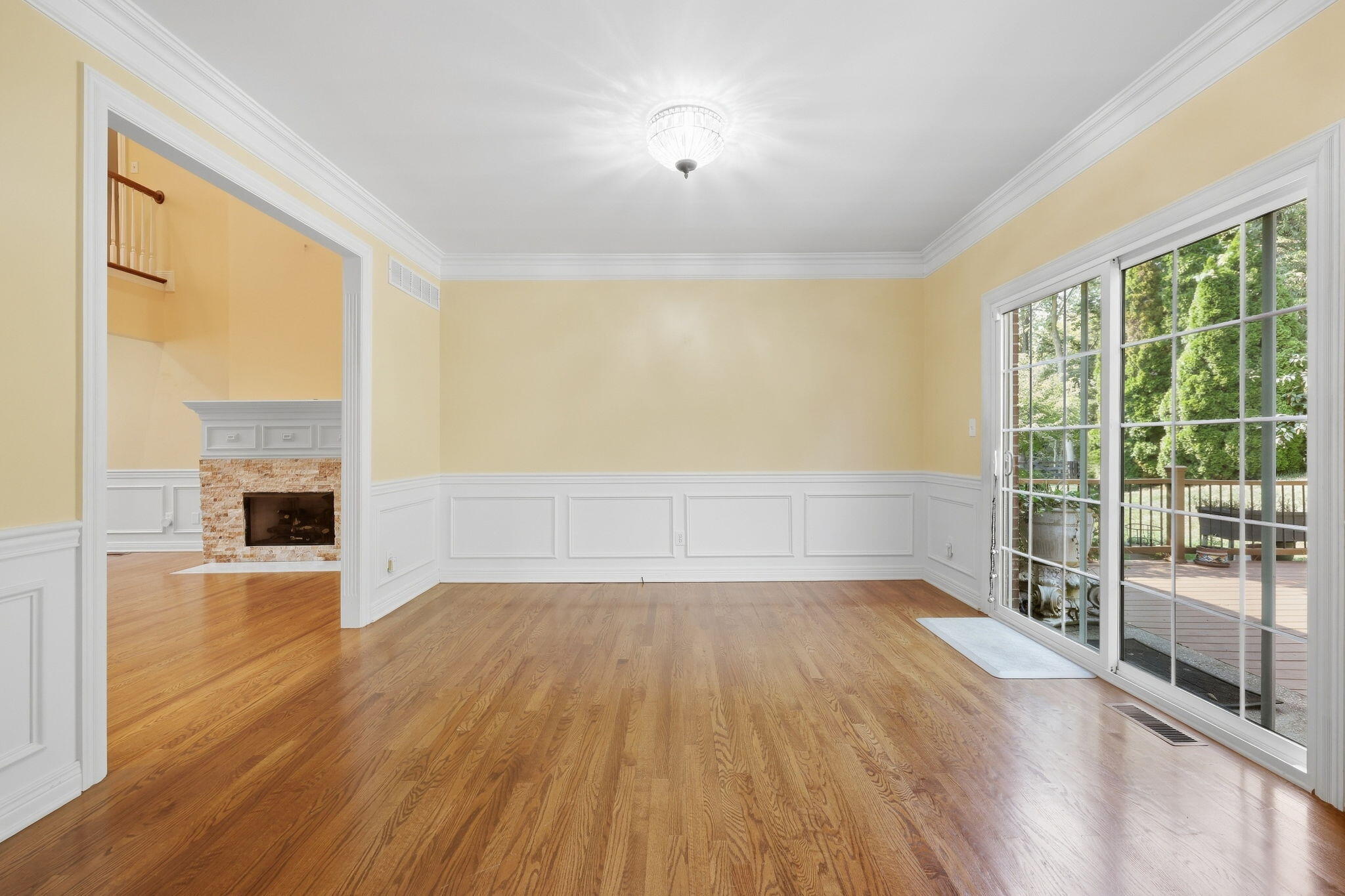 Empty room with hardwood floors and white wainscoting, opening to a deck through sliding glass doors.