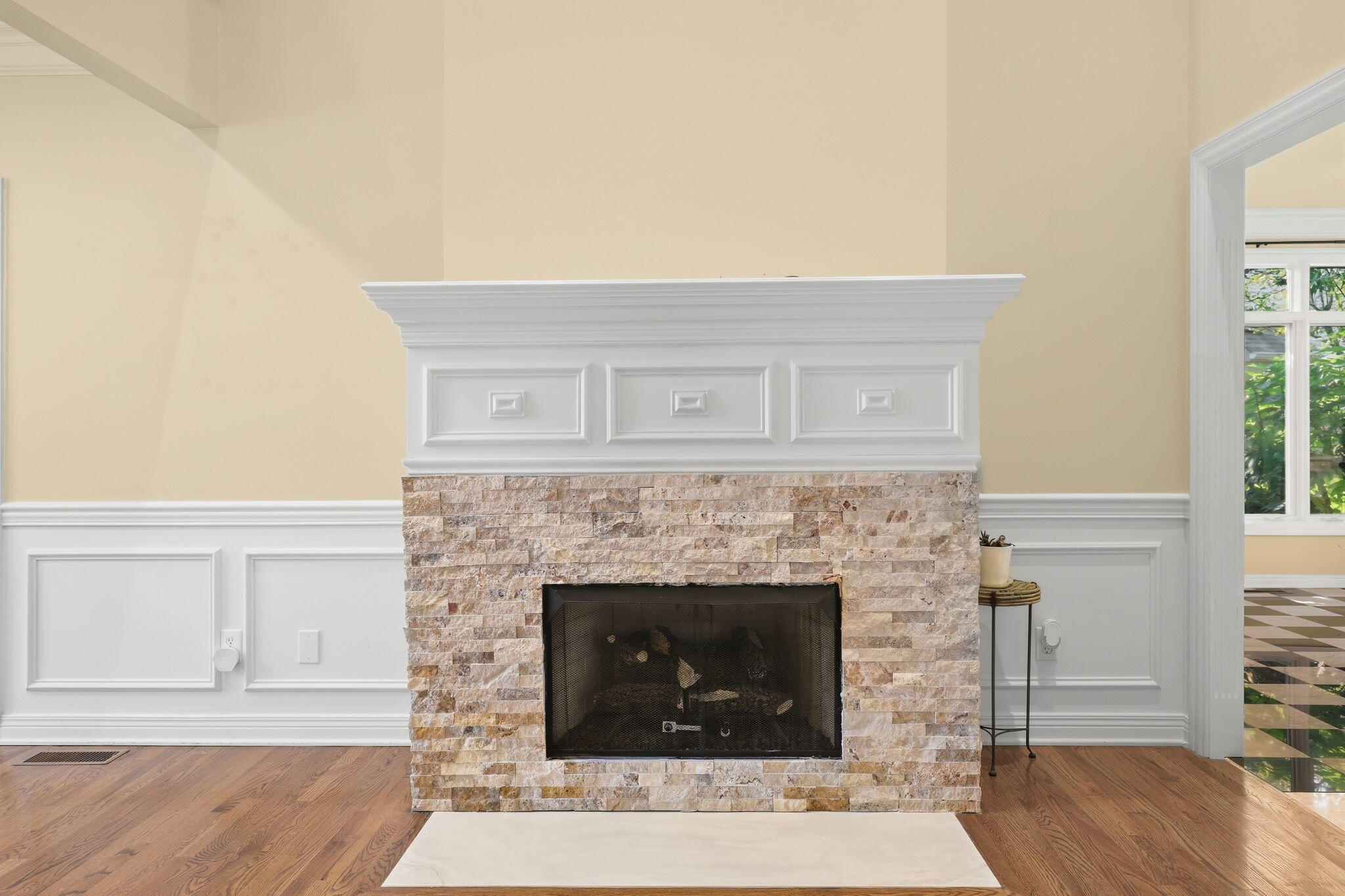 Stone fireplace with a white mantel and hearth, hardwood floors, and paneled walls.