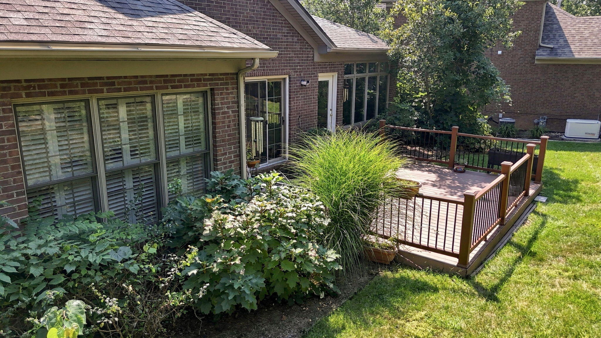 Brick home’s raised deck with black railings, surrounded by leafy shrubs and ornamental grass.