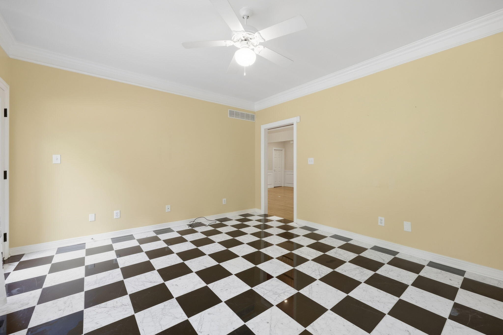 Empty room with a black-and-white checkerboard tile floor, pale yellow walls, and a ceiling fan.