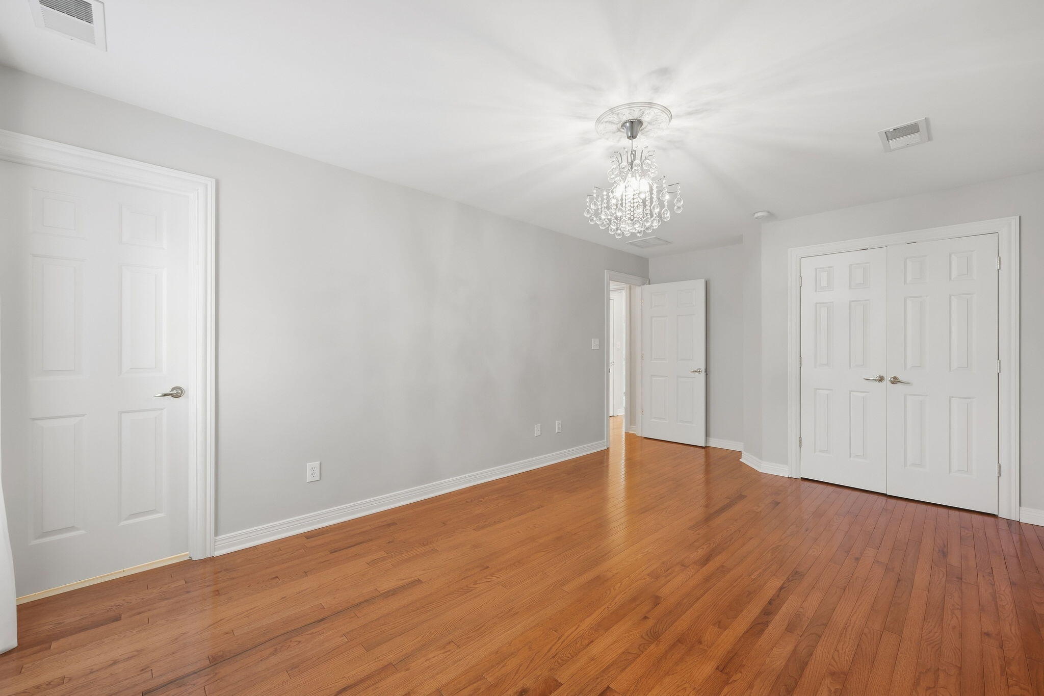 Empty bedroom with hardwood floors, white closet doors, and a crystal chandelier.