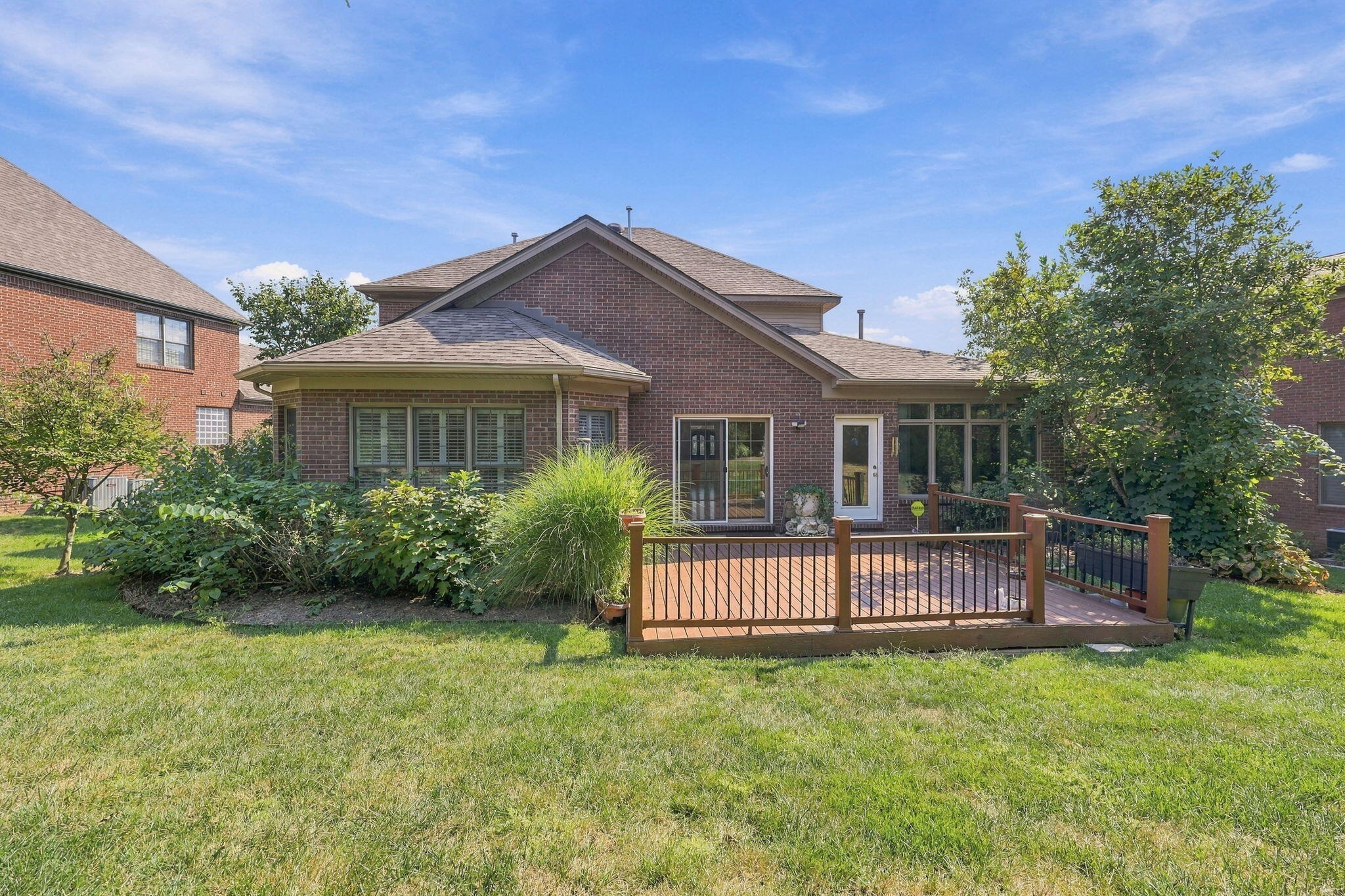 Brick home’s rear exterior with a raised deck, garden beds, and a broad lawn.