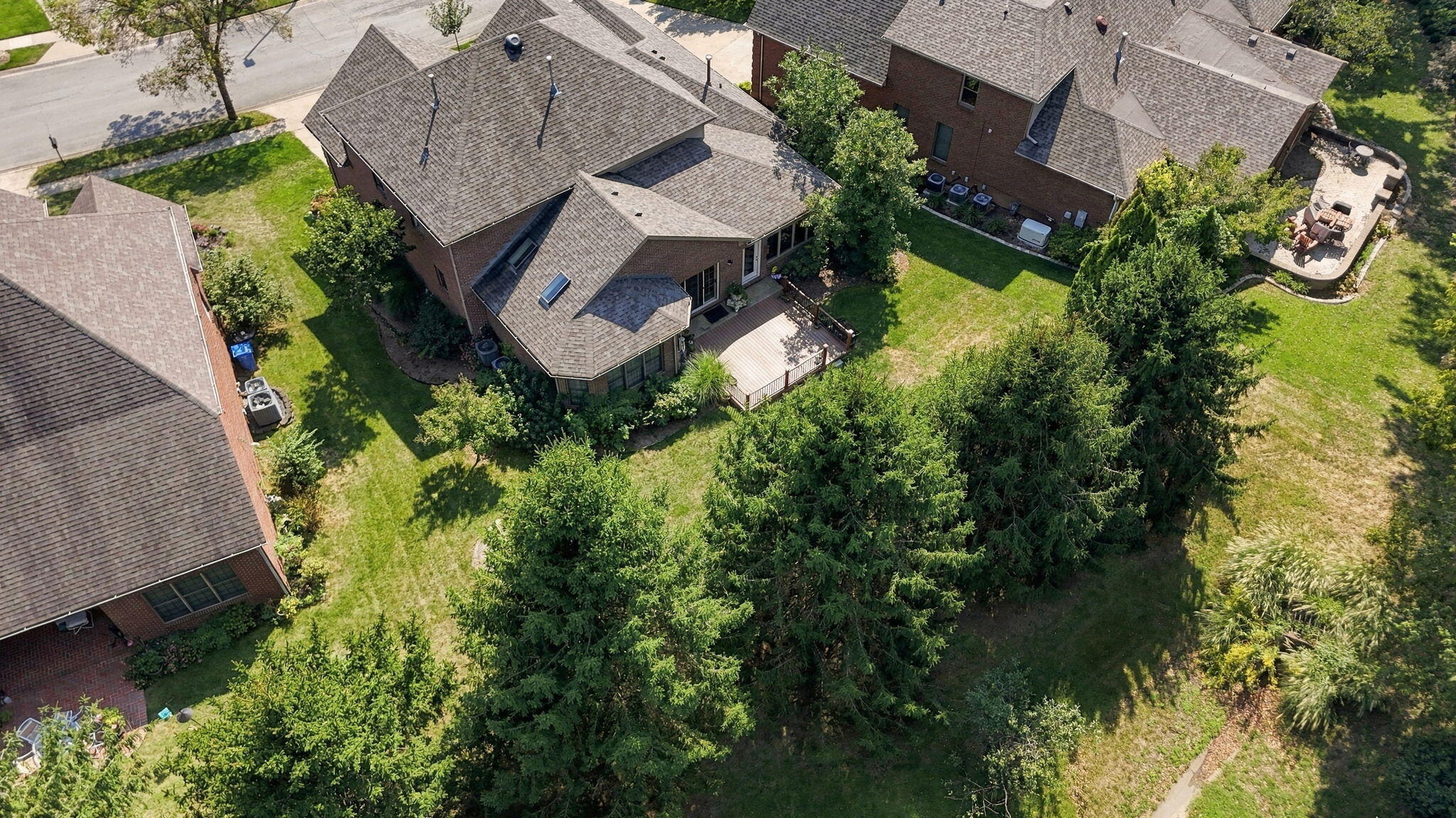 Aerial view of a brick home with a rear deck, landscaped yard, and separate outdoor patio.