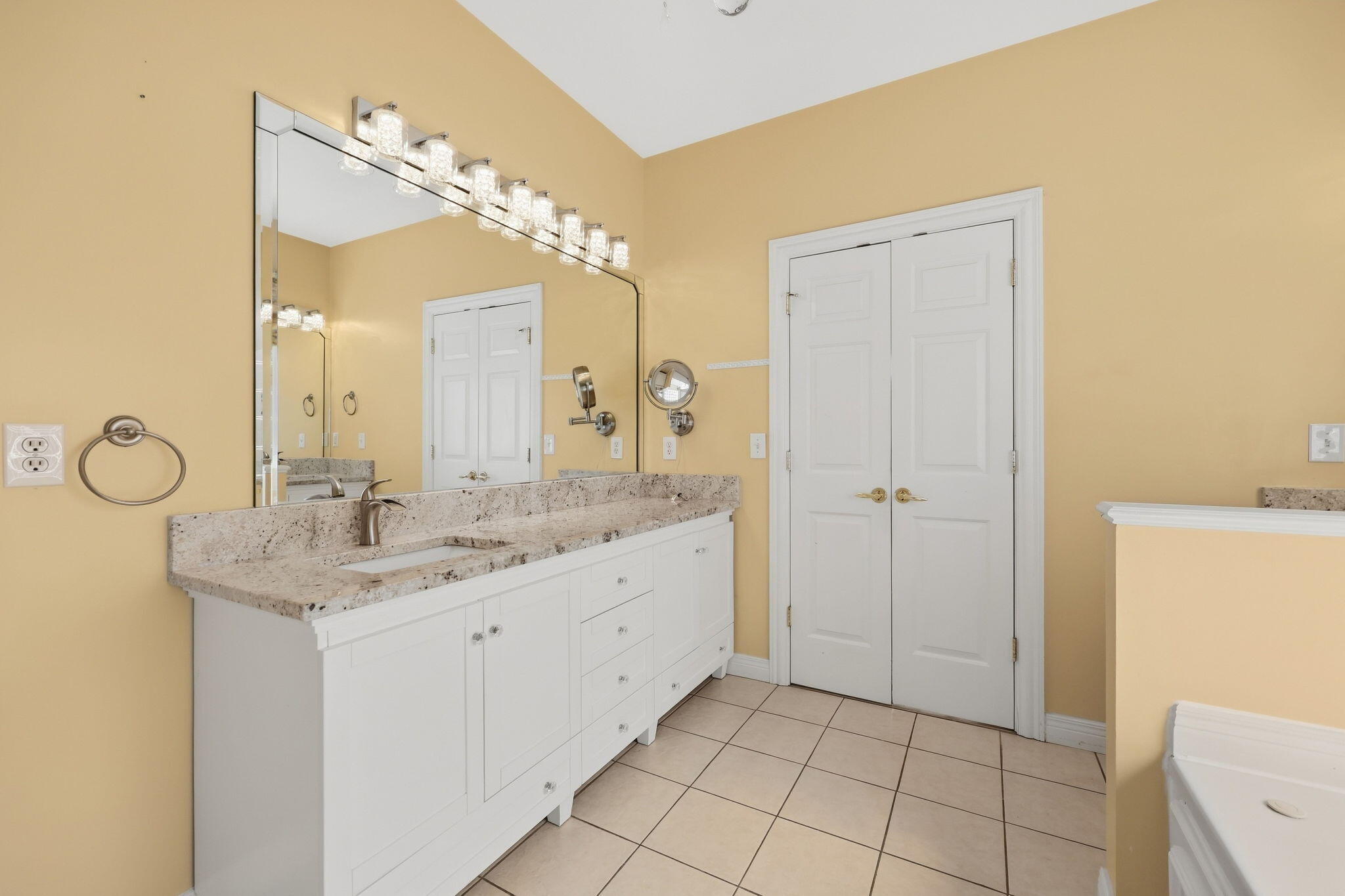 Bathroom with a long white vanity, stone countertop, oversized mirror, and double doors.