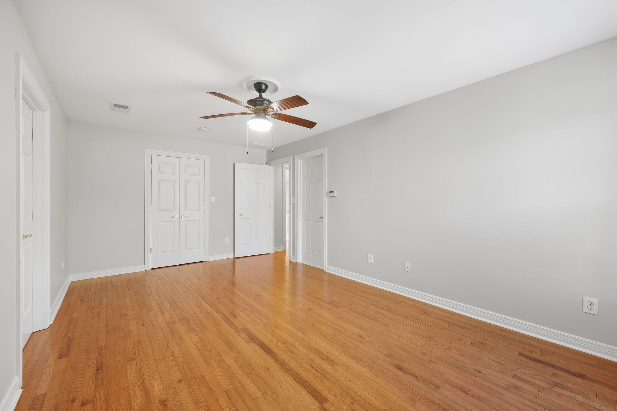 Empty bedroom with hardwood floors, double closet doors, and a ceiling fan.