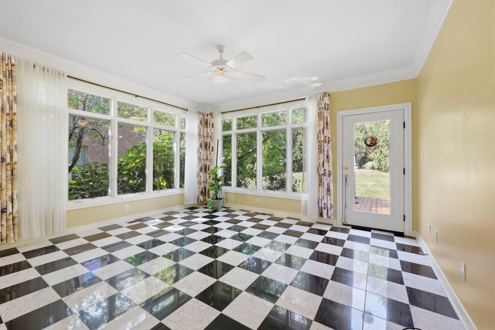 Sunroom with glossy checkerboard tile, expansive curtained windows, and a glass-panel door to the yard.