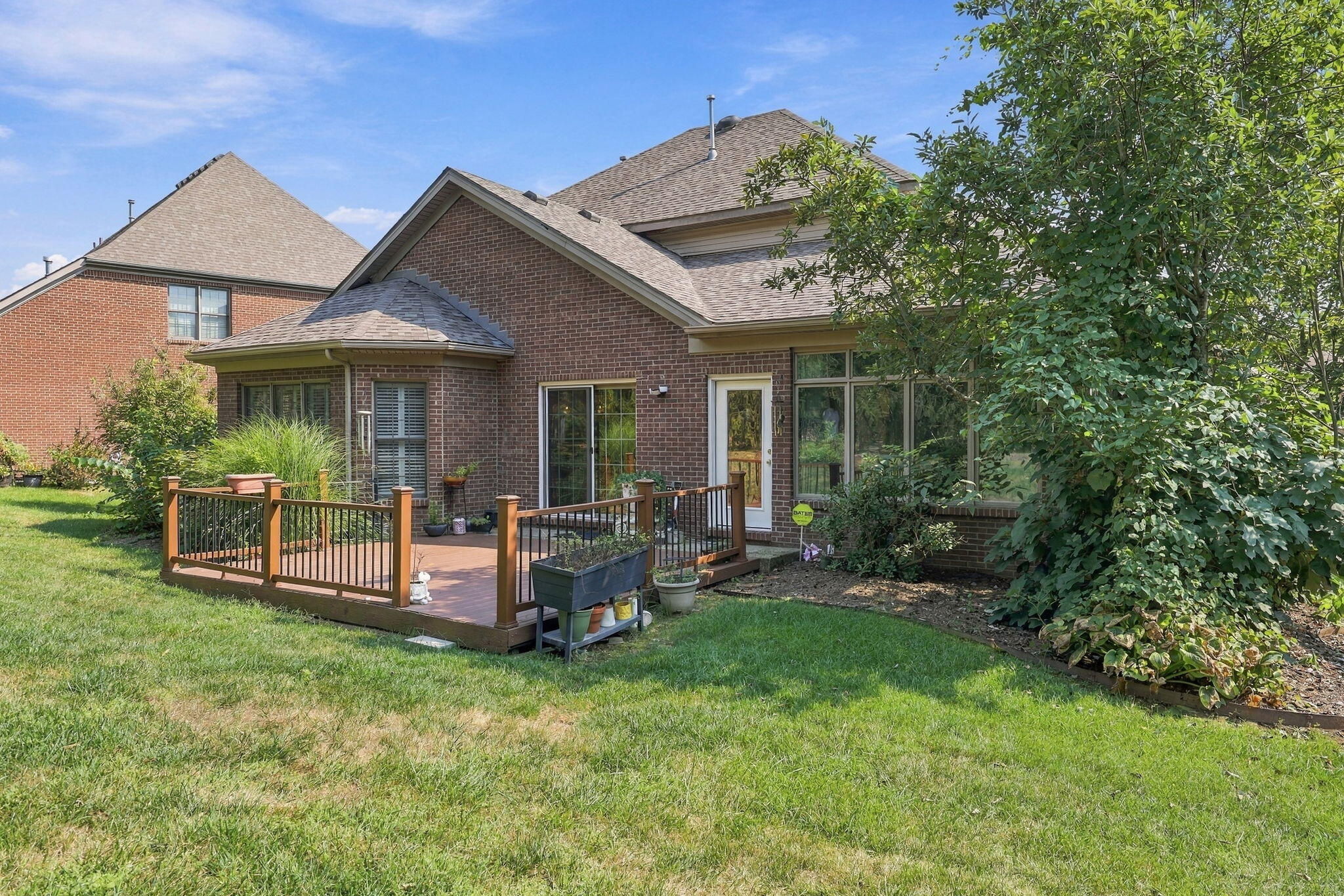 Brick house rear exterior with a raised deck, black railings, and a leafy lawn.