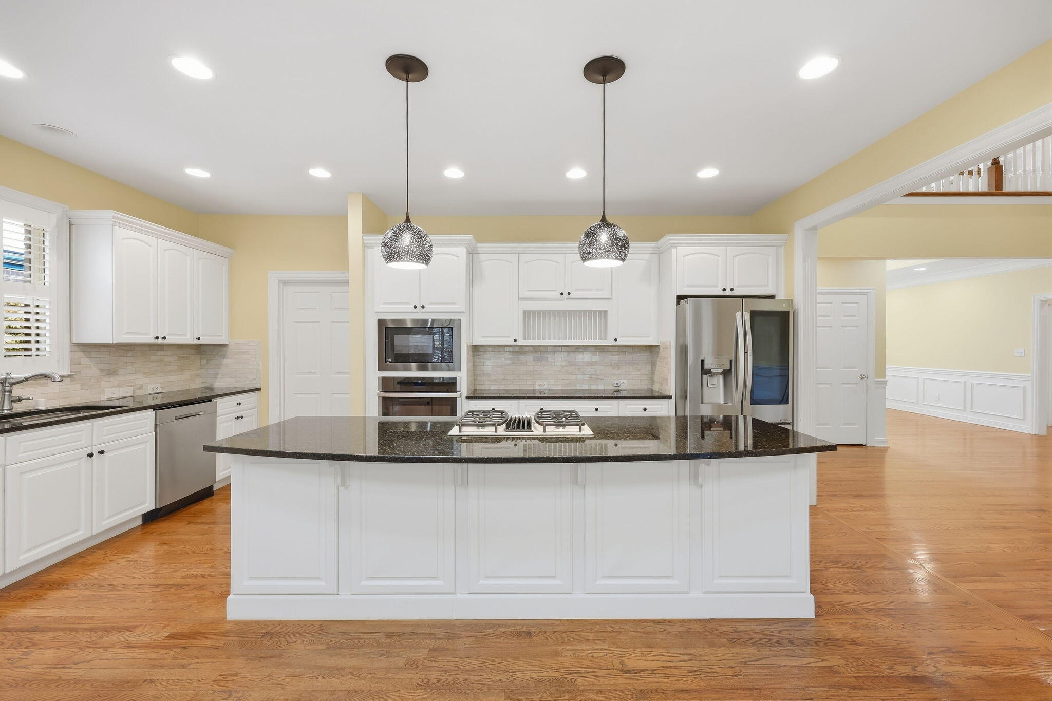 Kitchen with a large granite island, white cabinetry, stainless steel appliances, and hardwood floors.