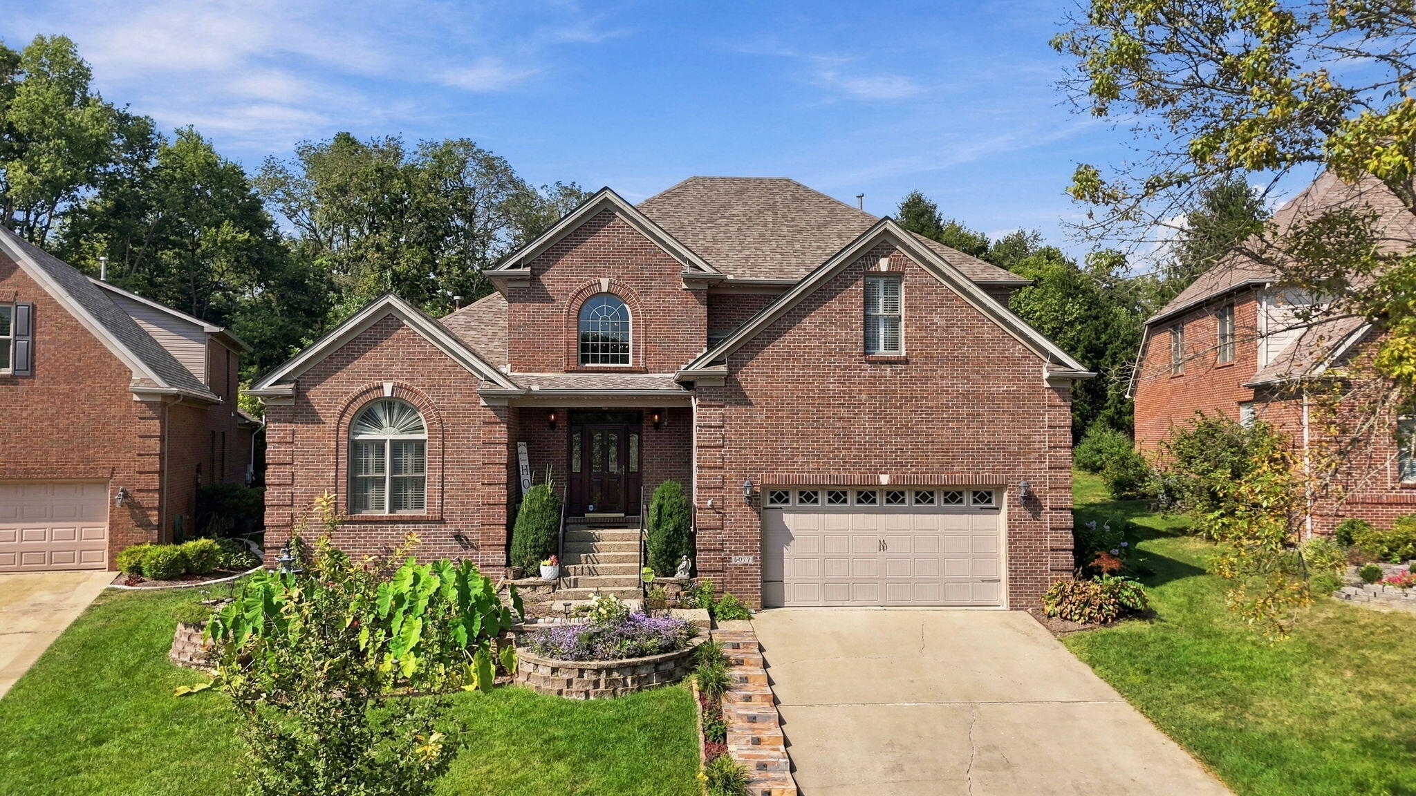 Two-story red brick home with arched windows, a two-car garage, and landscaped front garden.