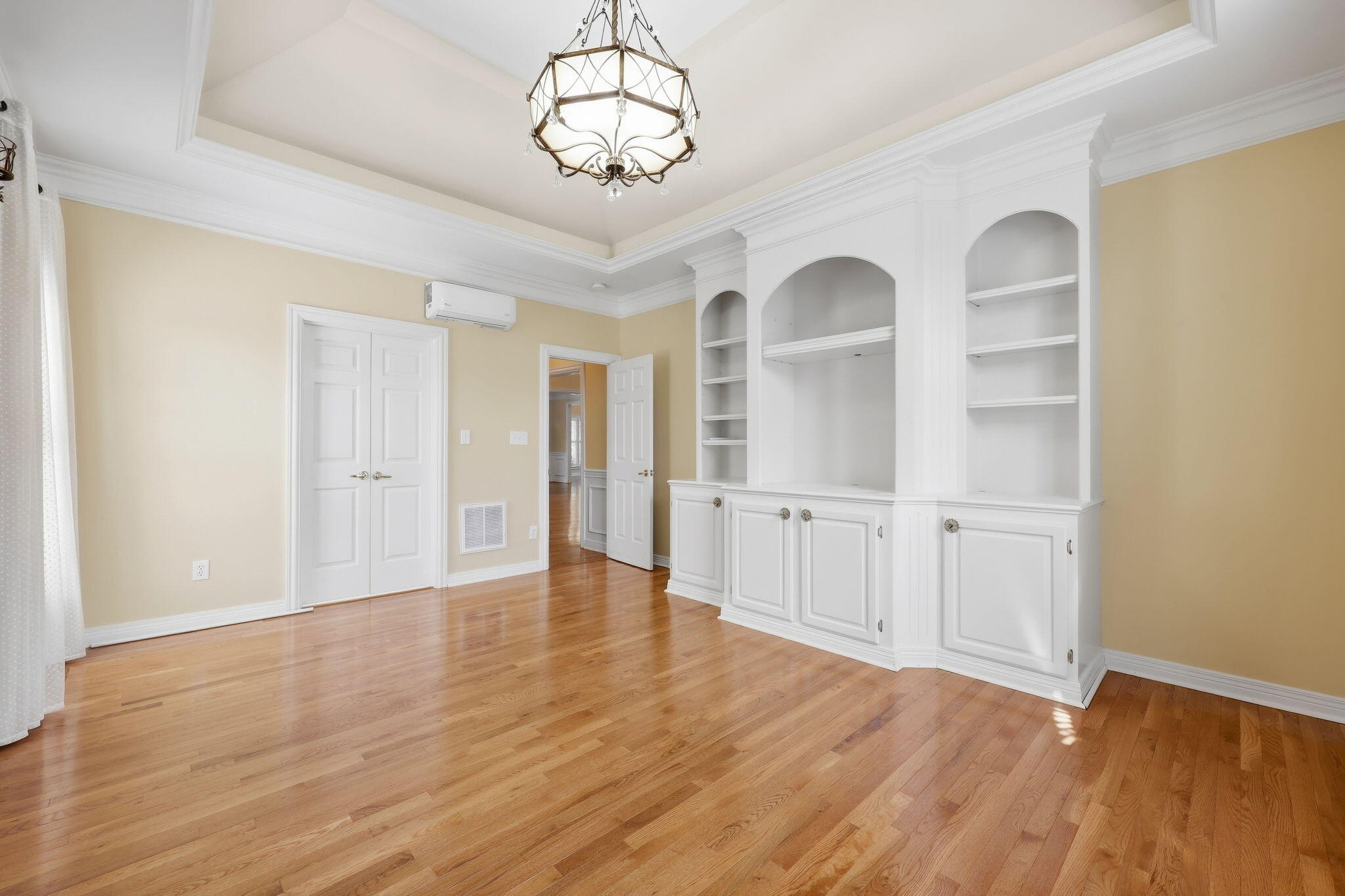 Empty room with hardwood floors and white built-in cabinets with arched shelves.