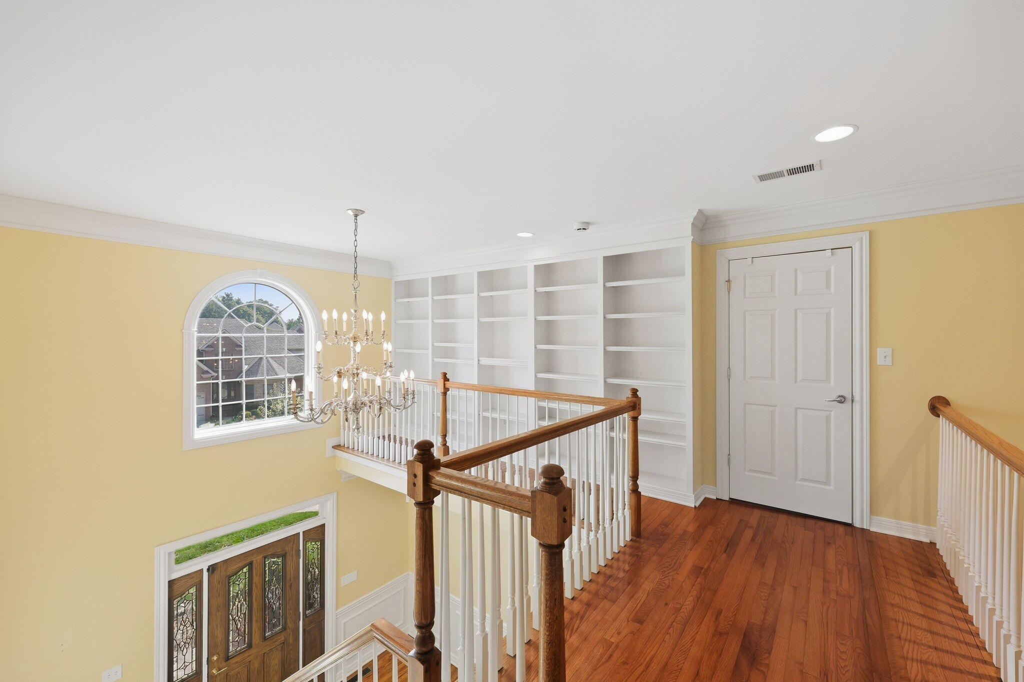 Upstairs landing with built-in bookshelves, hardwood floors, and an arched window overlooking the foyer.