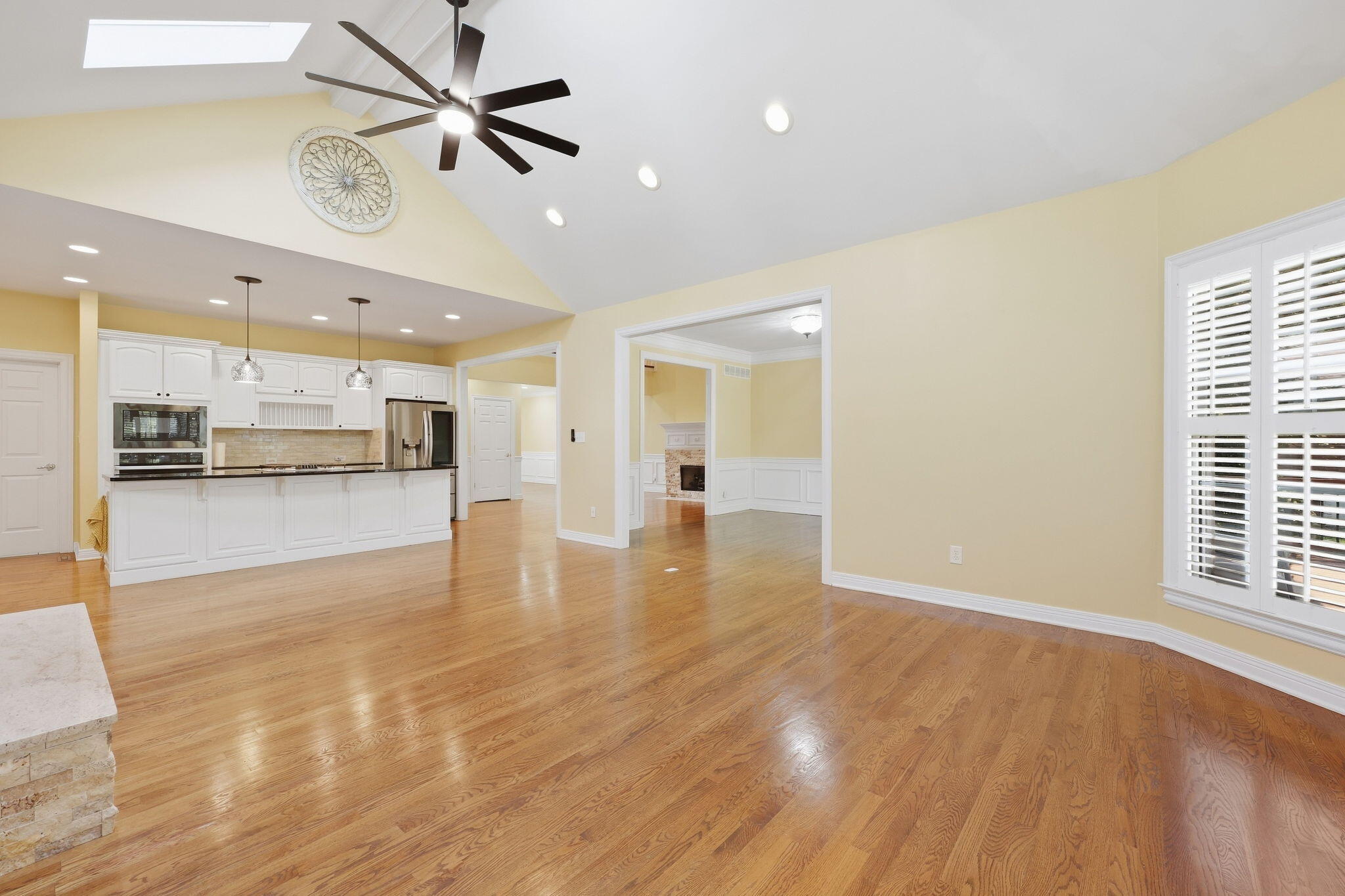 Open kitchen and dining area with white cabinetry, hardwood floors, a vaulted ceiling, and plantation shutters.