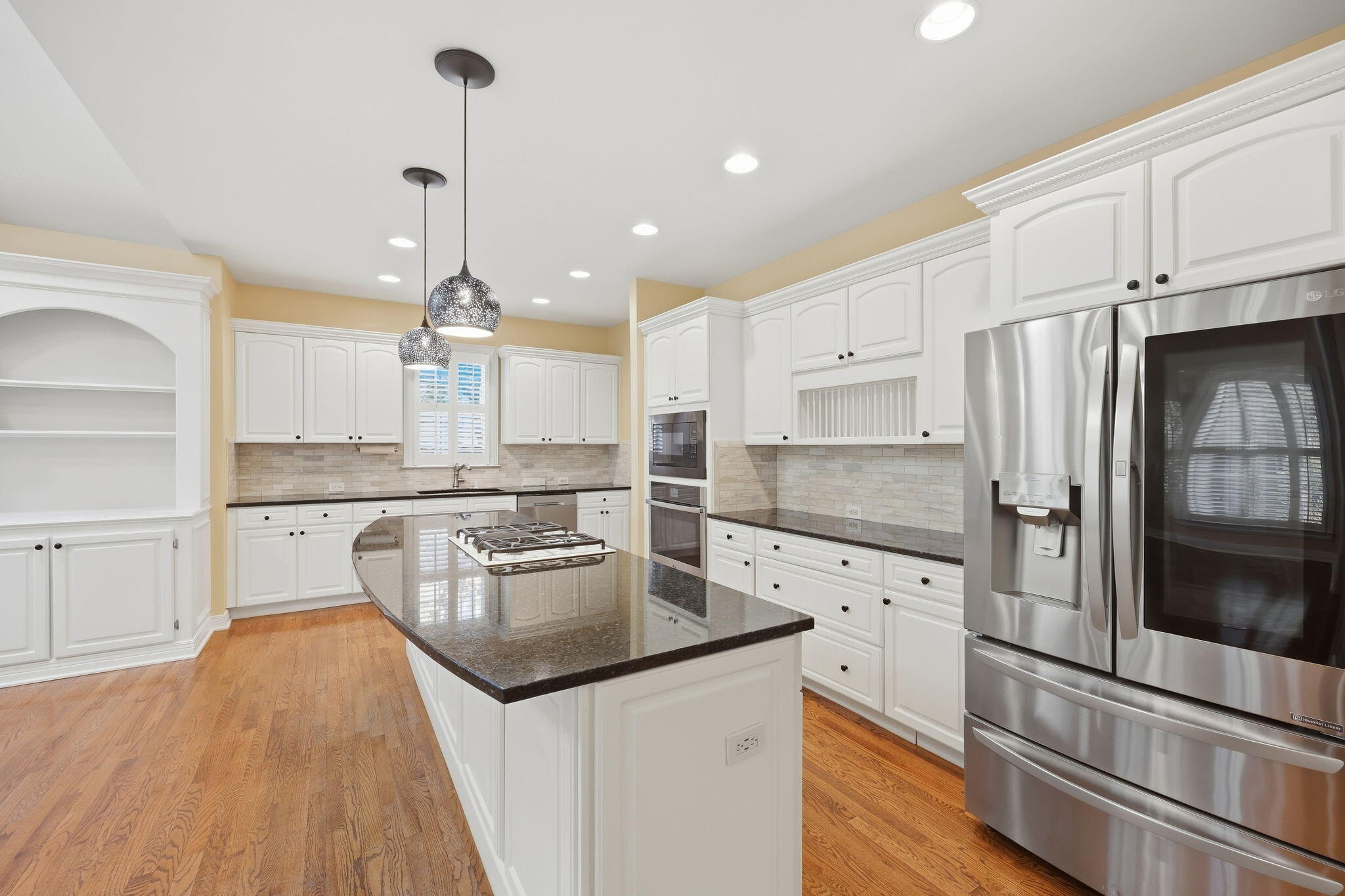 Kitchen with a granite cooktop island, white cabinetry, stainless steel appliances, and hardwood floors.