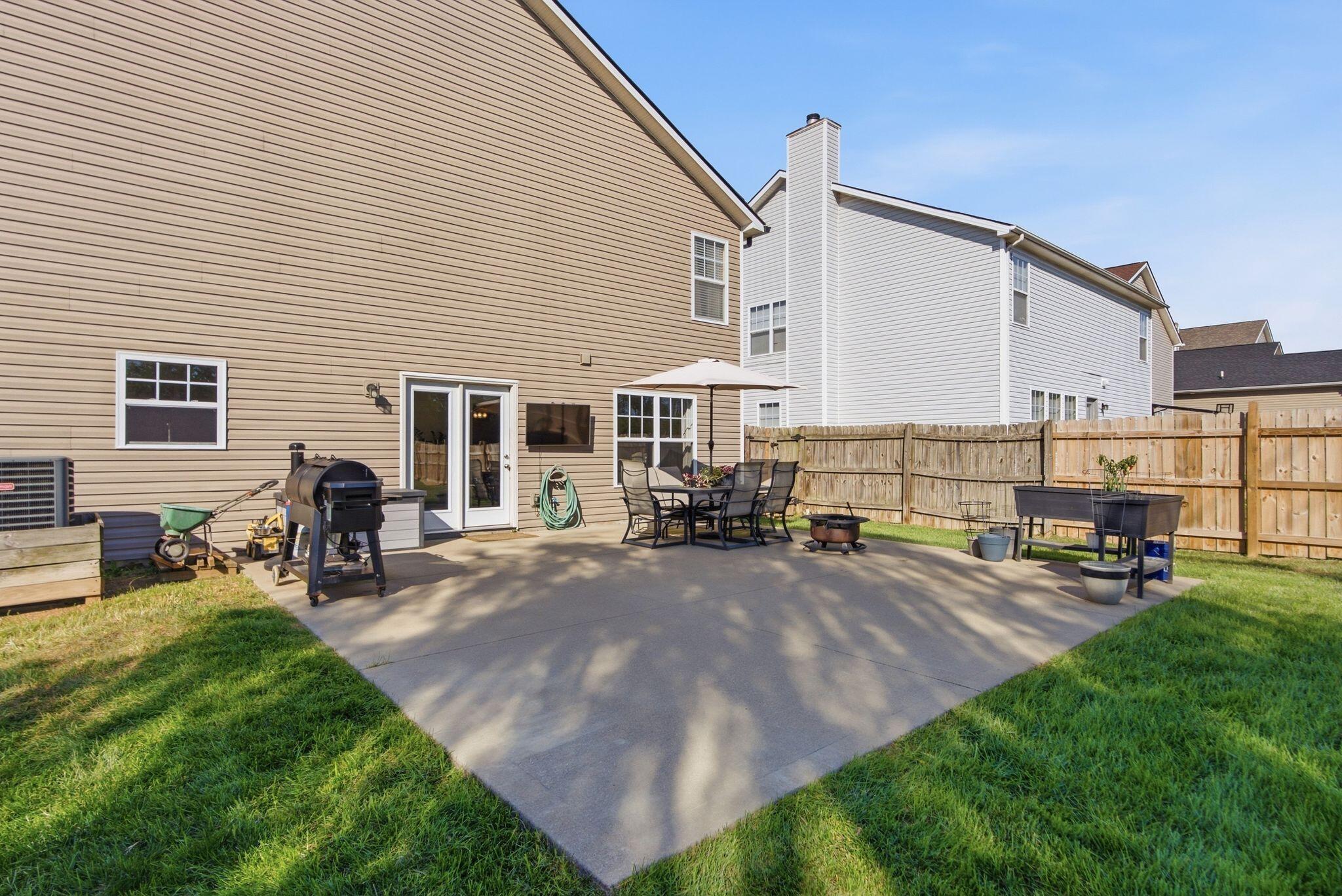Backyard patio with umbrella-covered dining set, grill, raised planters, and wooden privacy fence.