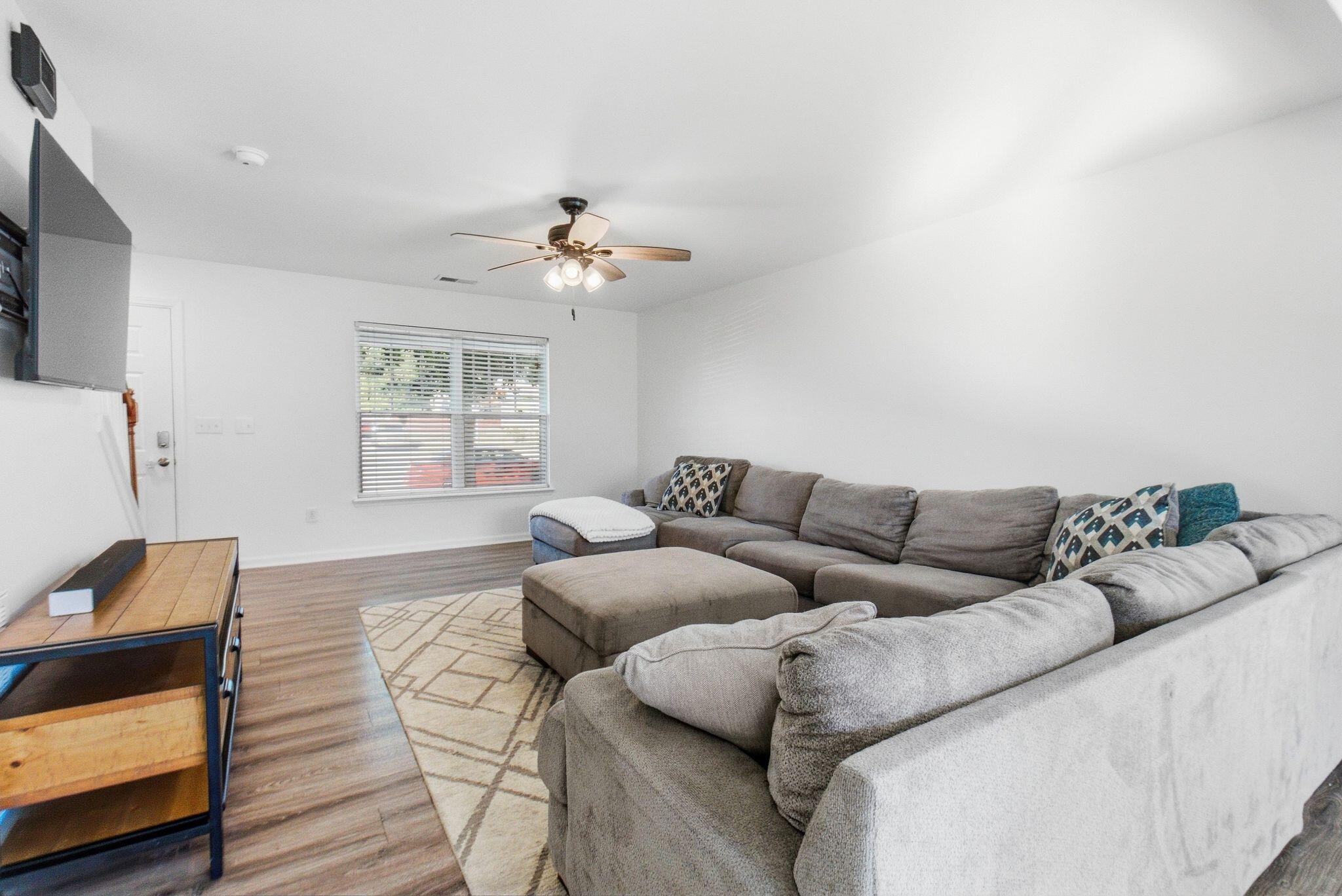 Living room with a gray sectional sofa, patterned rug, and ceiling fan.