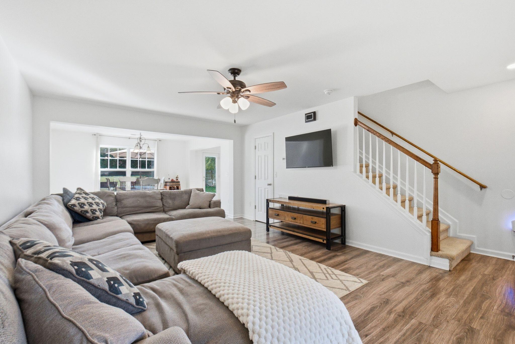 Living room with a gray sectional, wall-mounted TV, and staircase with a wood handrail.