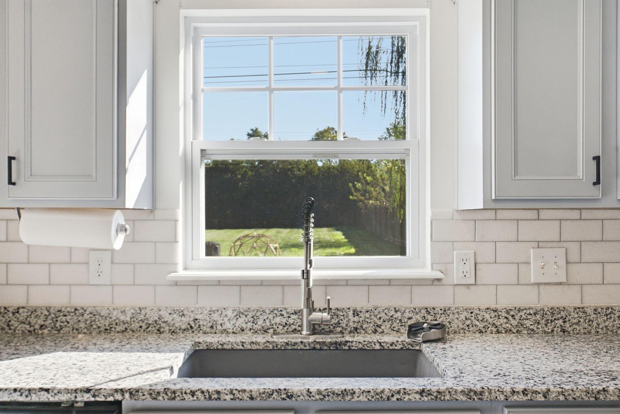 Kitchen sink with a spring-coil faucet beneath a large window and speckled granite counters.