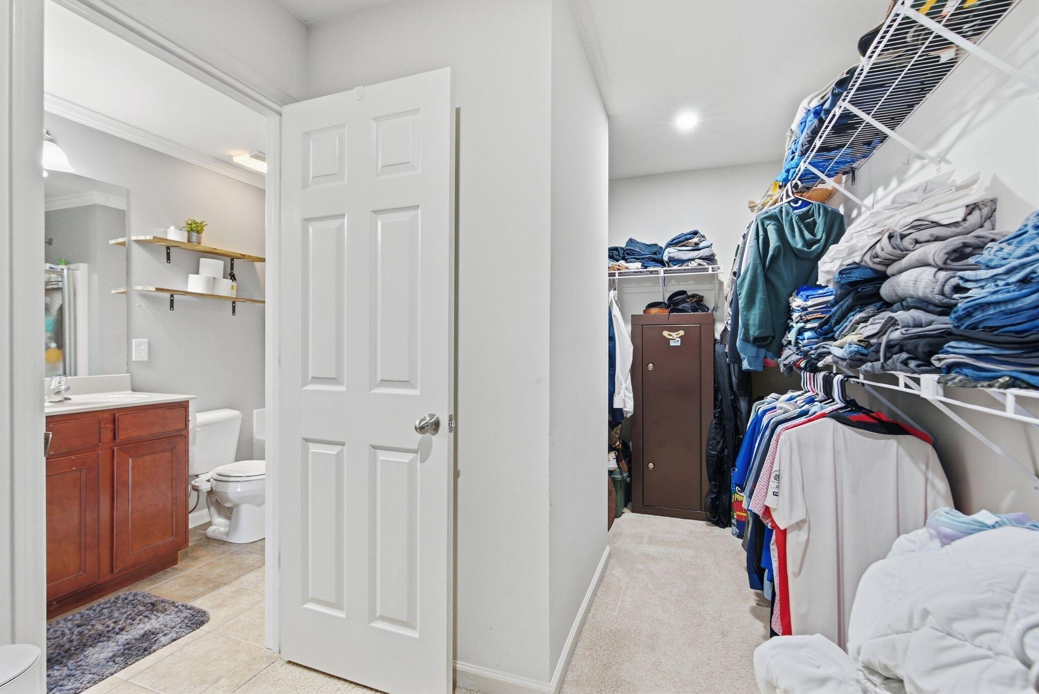 Walk-in closet with clothing shelves beside an adjoining bathroom with a wood vanity and tile floor.