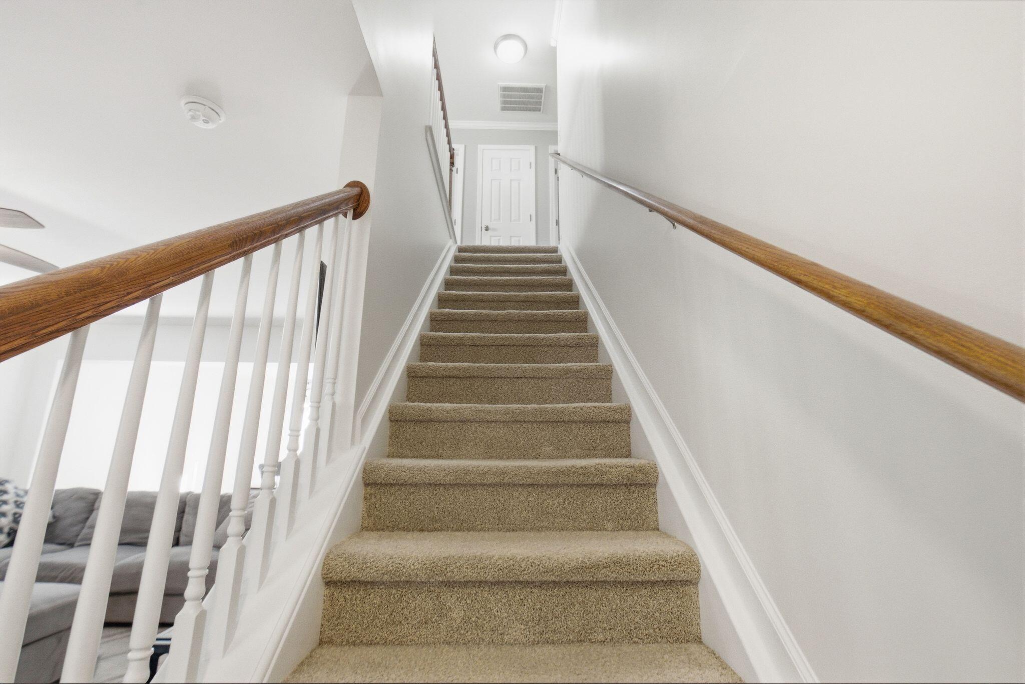 Carpeted staircase with wooden handrails and white balusters leading to an upstairs landing.